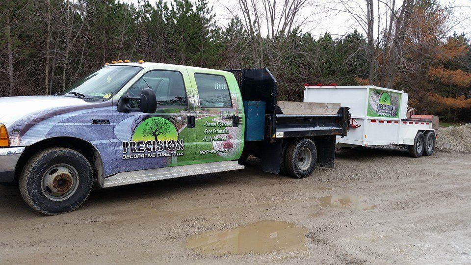 A dump truck with a trailer attached to it is parked in a dirt lot.