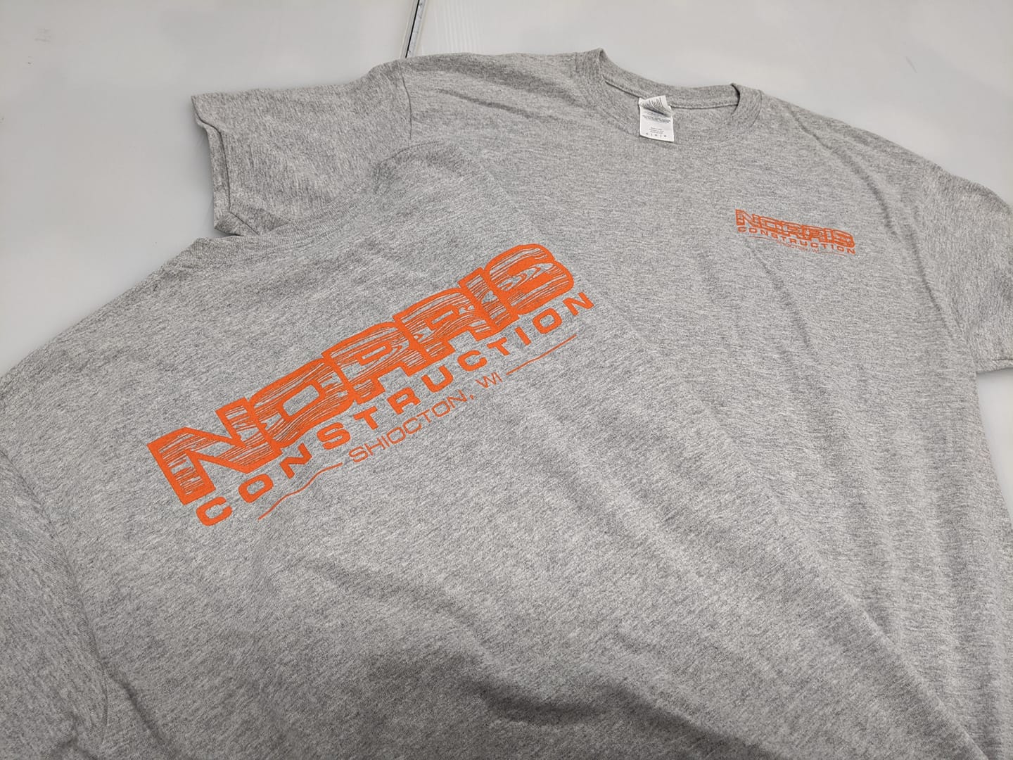 A grey t-shirt with orange writing on it is sitting on a table.