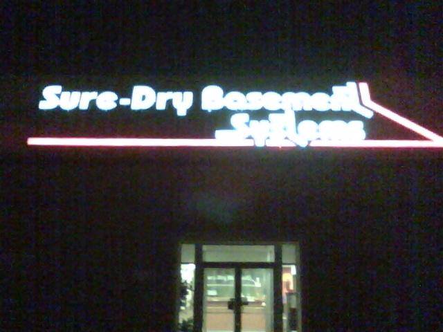 A store front with a neon sign that says sure-dry basement systems