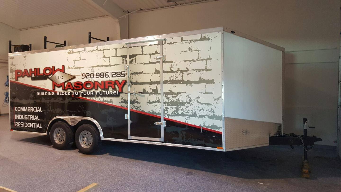 A white trailer with a brick wall on the side is parked in a garage.