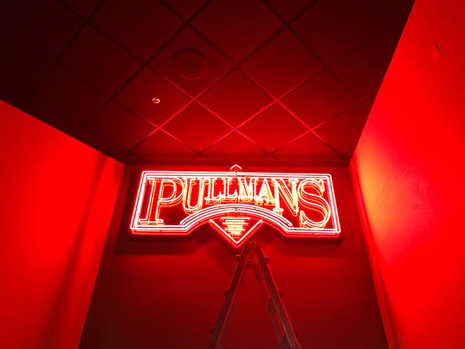 A neon sign that says pullans is lit up in a dark room.