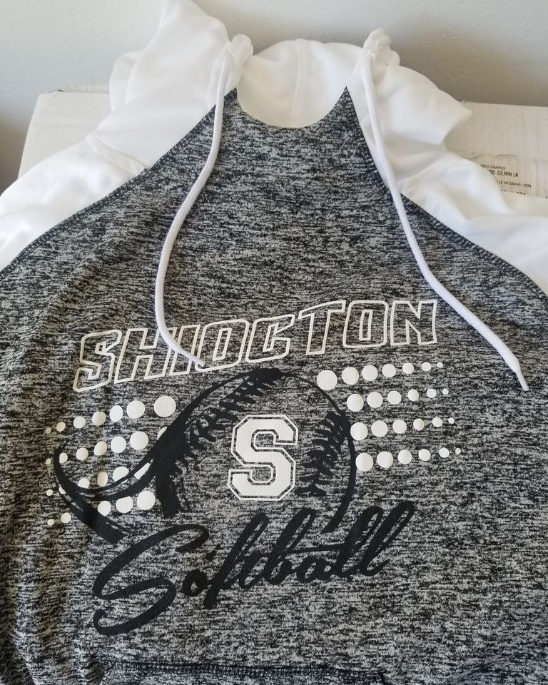 A gray and white softball hoodie is sitting on a table.