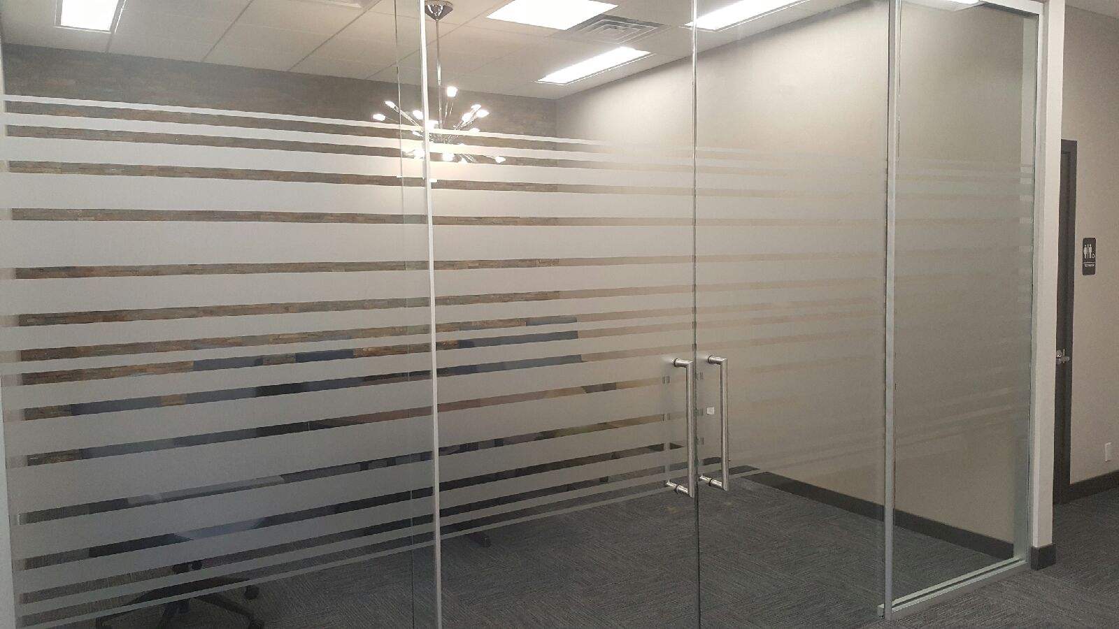 A room with a glass door and a striped window film on the wall.