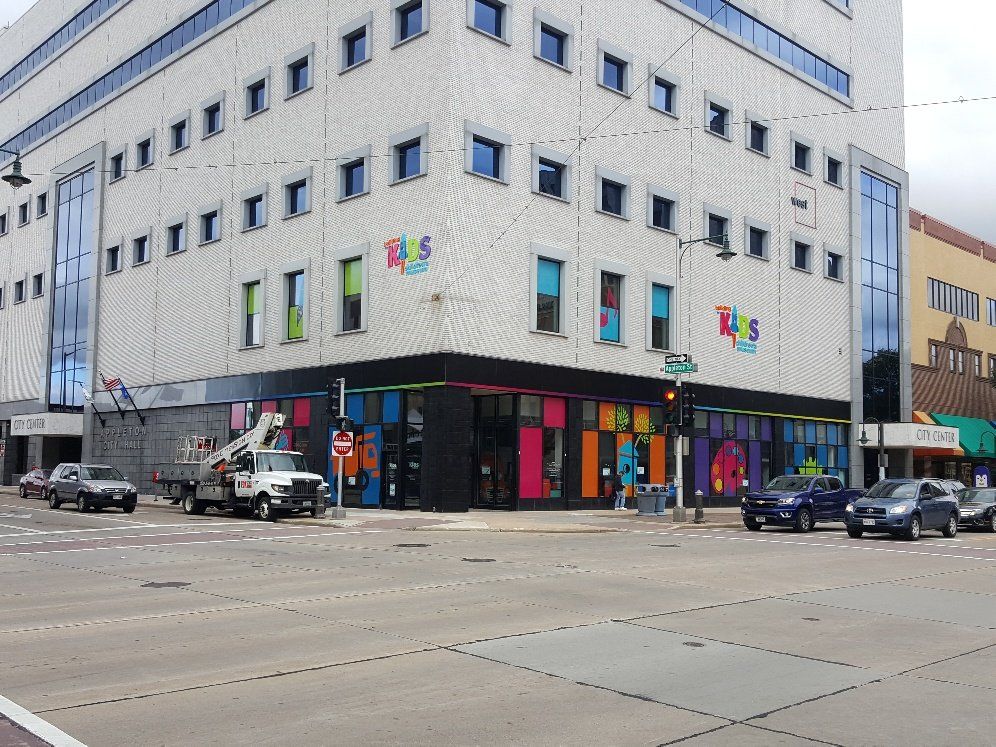 A large building with a lot of windows is on the corner of a city street.