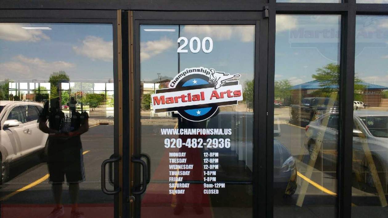 A man is standing in front of a glass door with a martini arts sign on it.