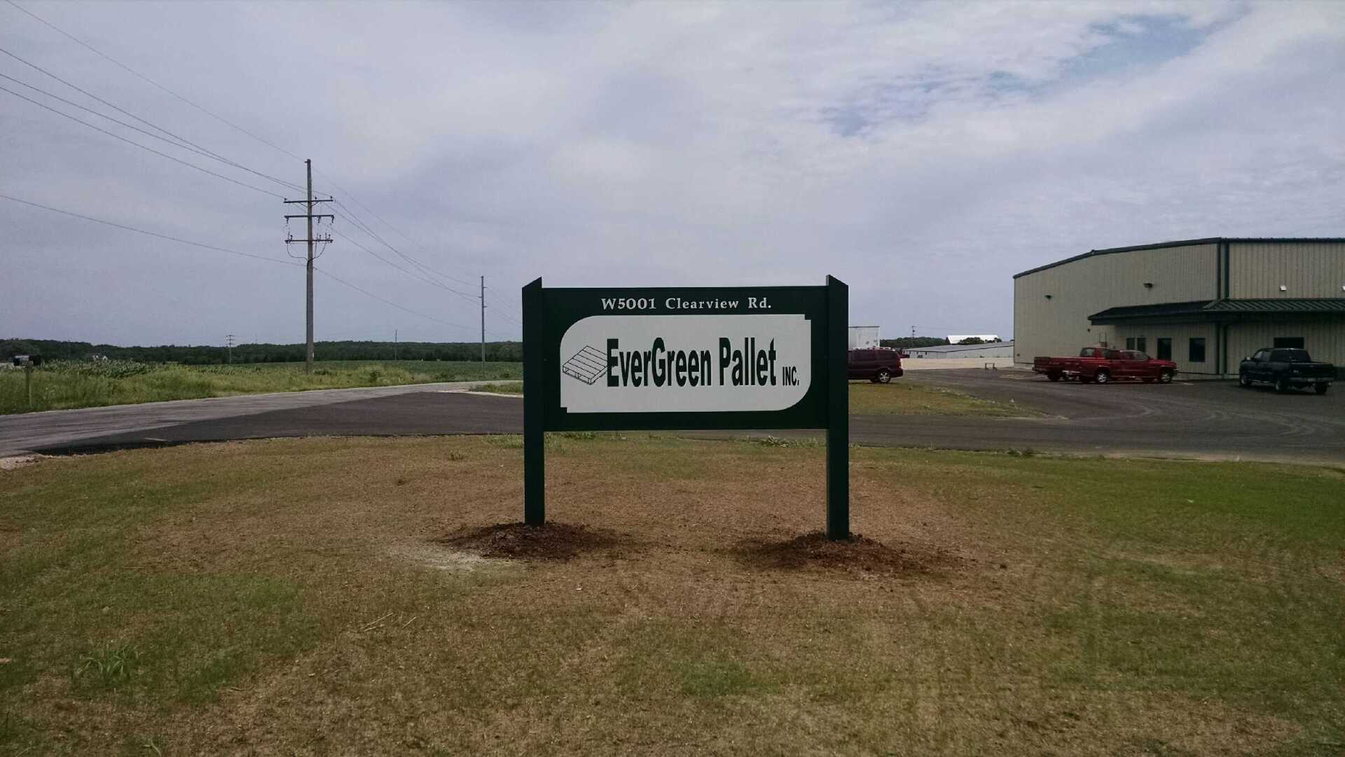 A green sign in the middle of a grassy field with a building in the background.