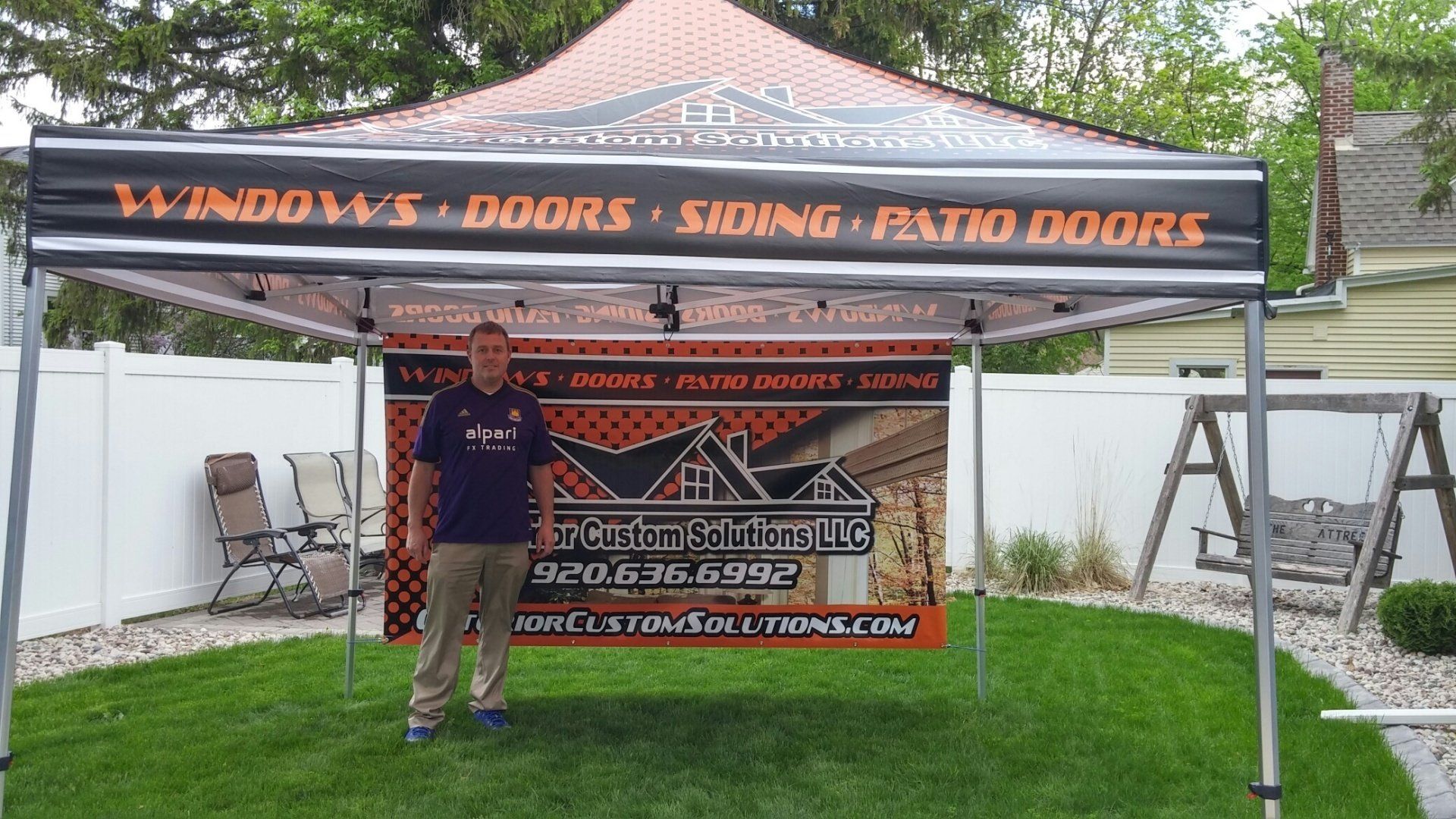 A man standing under a tent that says windows doors siding patio doors
