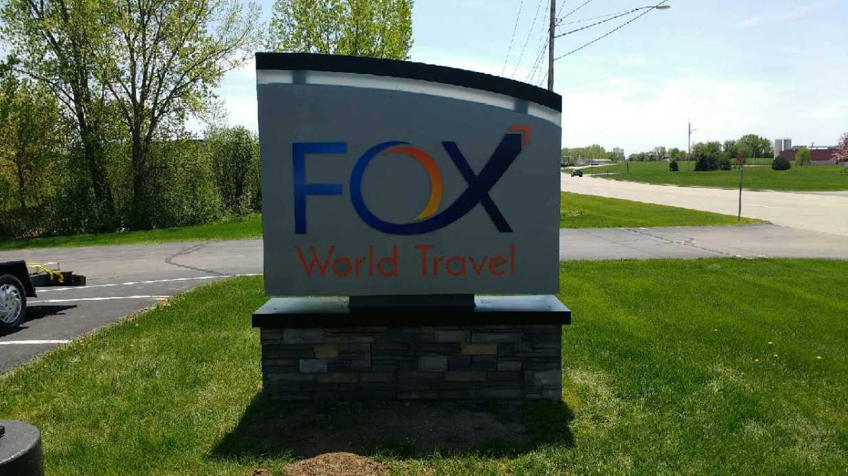 A sign for fox world travel is sitting in the grass.