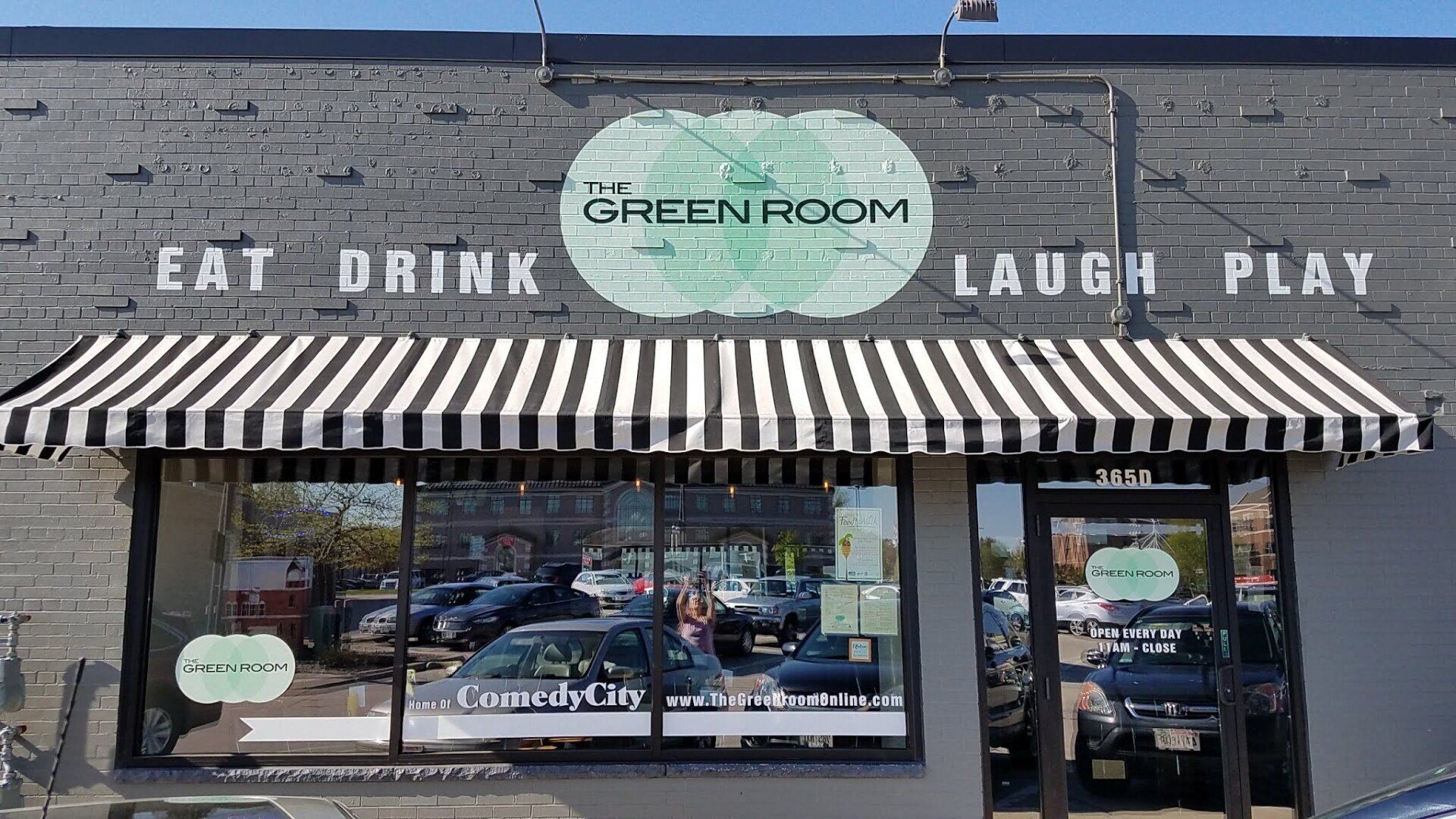 The front of a restaurant with a striped awning that says eat drink laugh play.