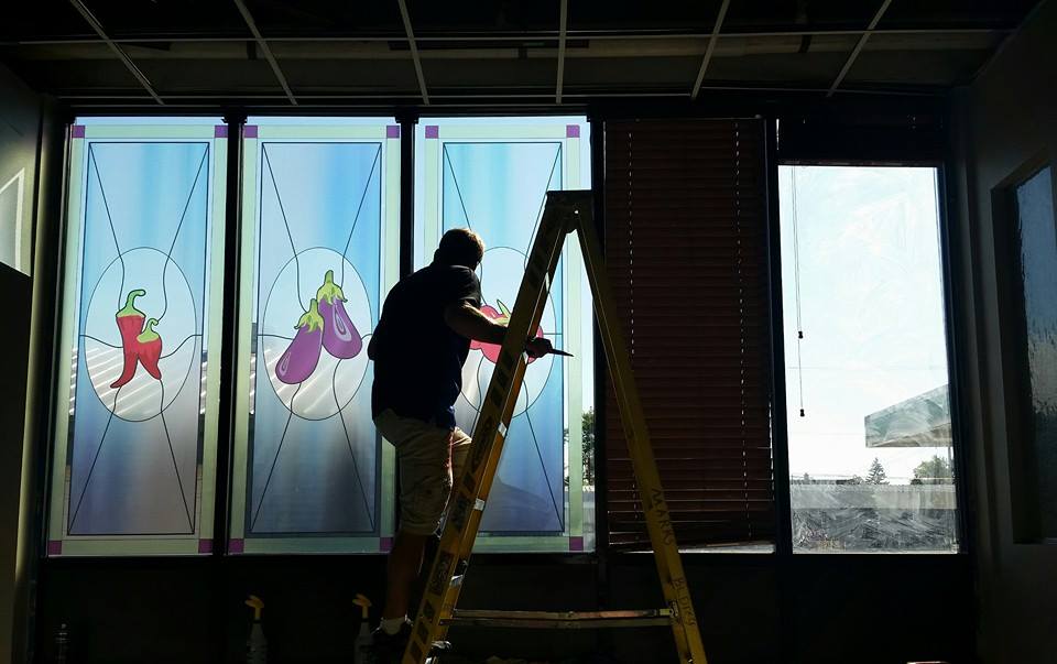 A man is standing on a ladder painting a stained glass window.