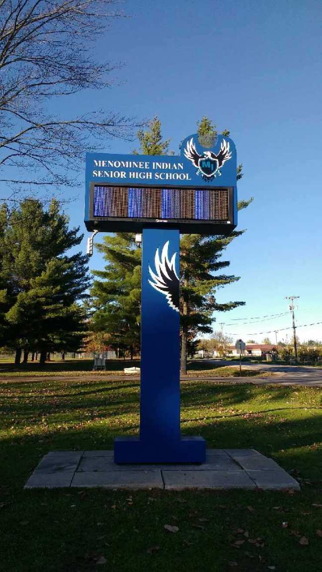 A blue sign with a bird on it is in a park.