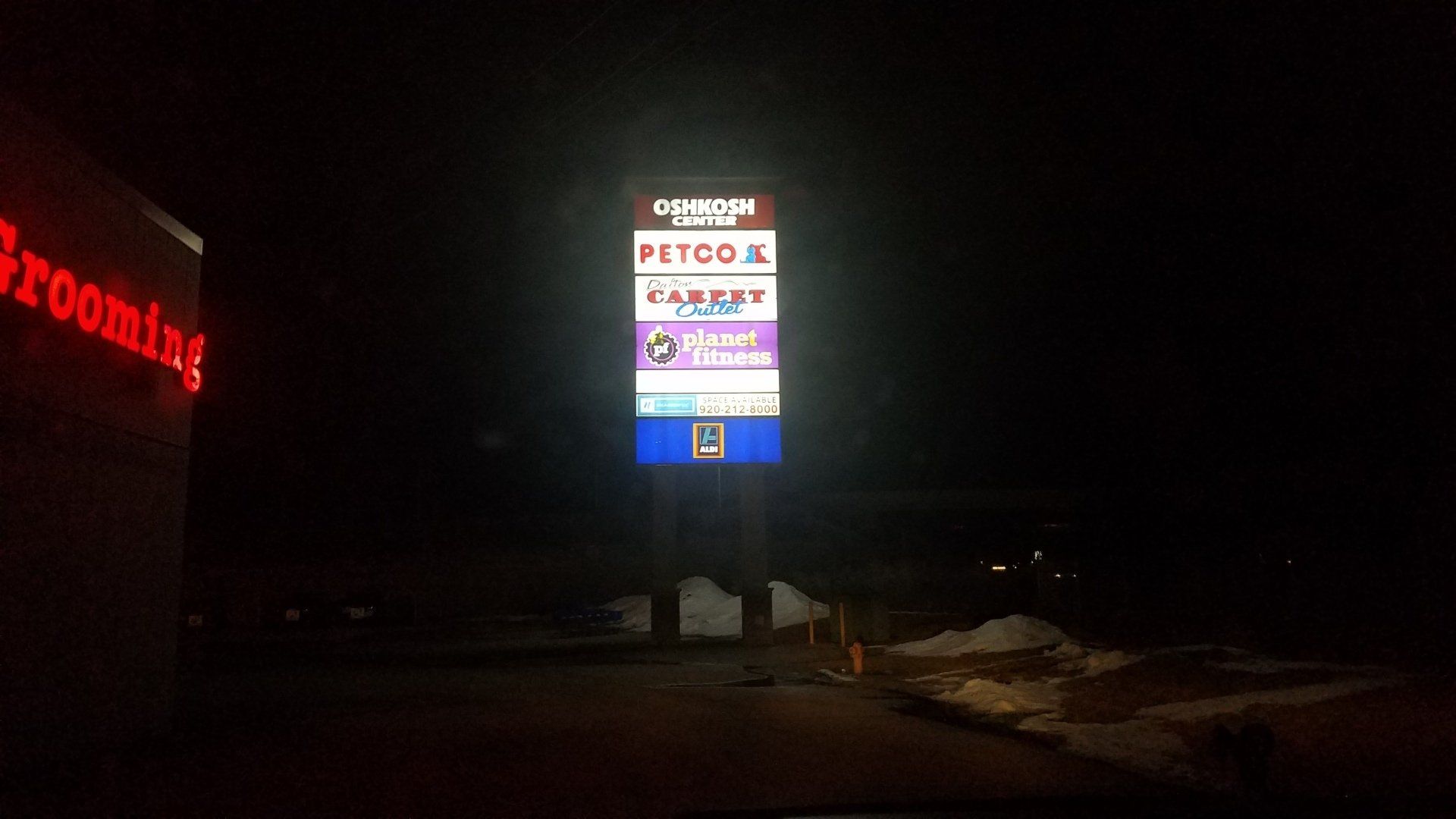 A large billboard is lit up at night in front of a petco store.