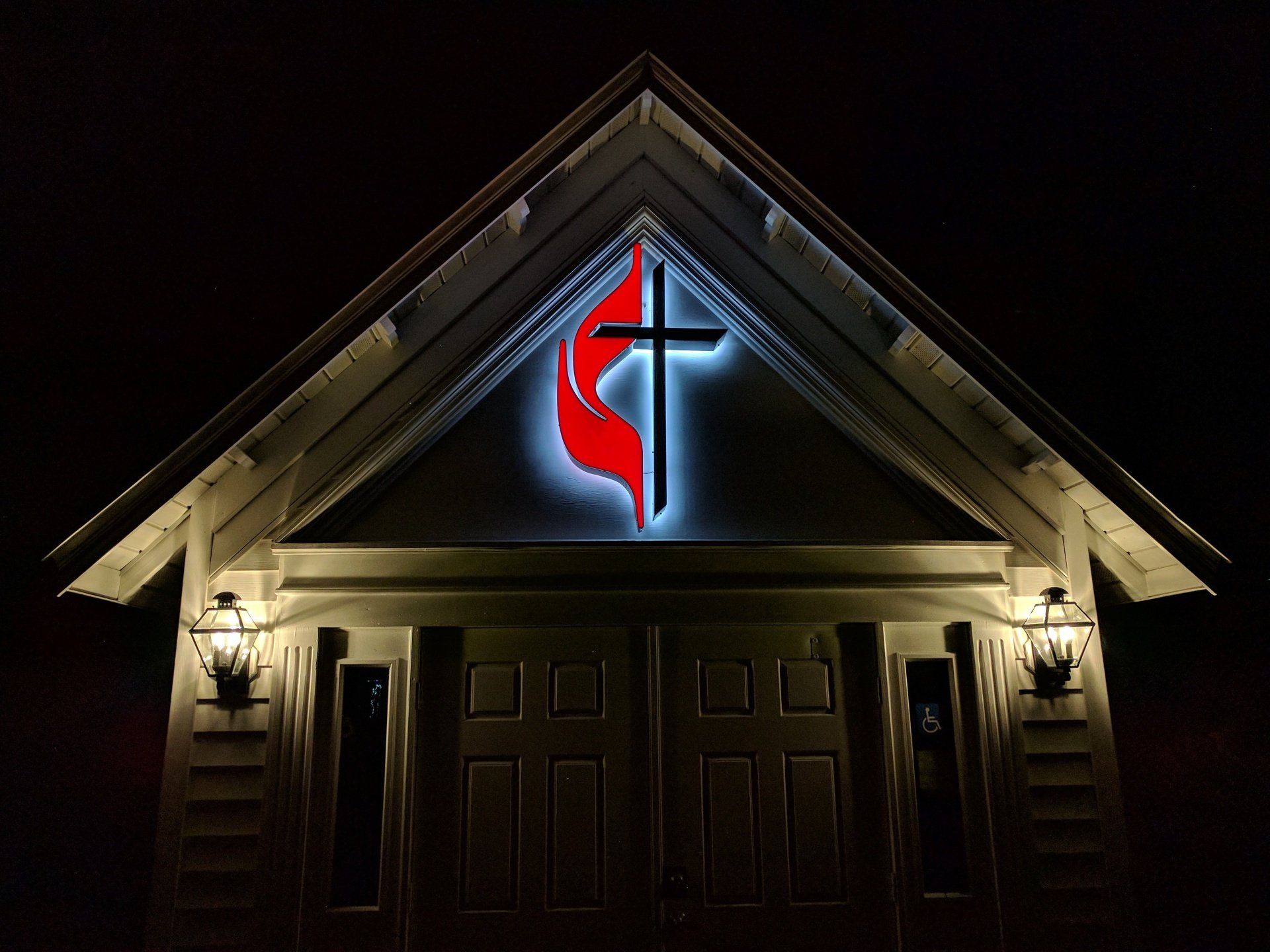A church with a cross and a flame on it is lit up at night.