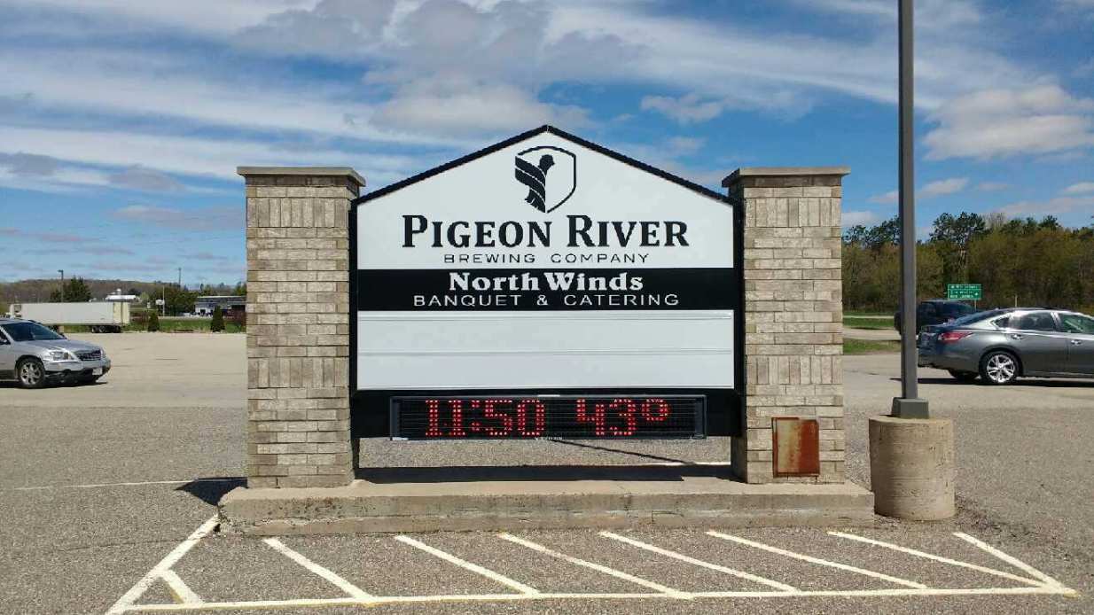 A pigeon river sign is in a parking lot with cars parked in front of it.