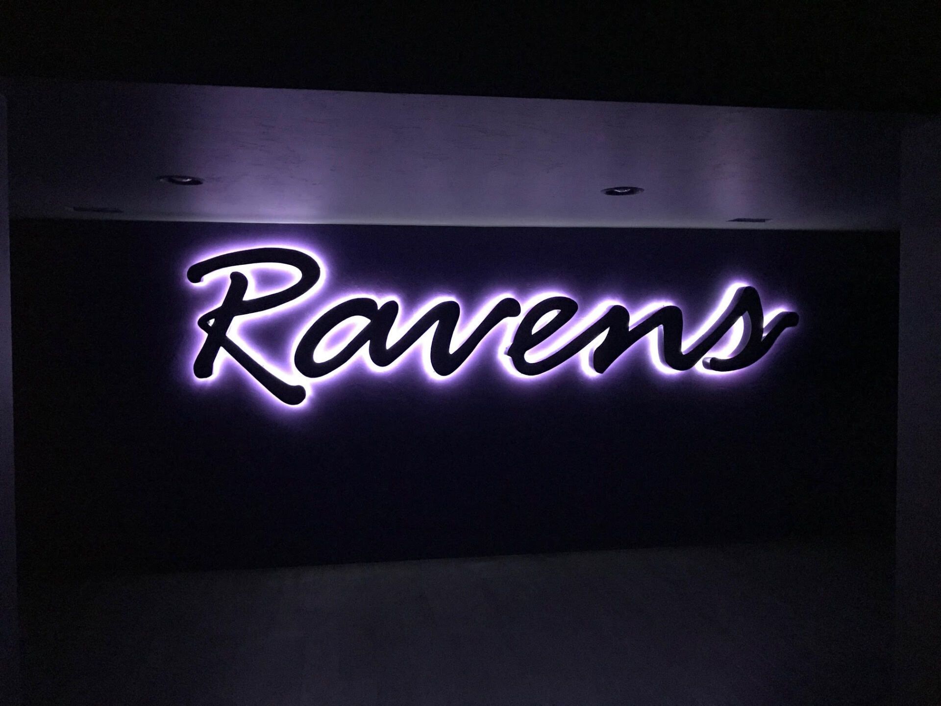 A sign that says ravens is lit up at night