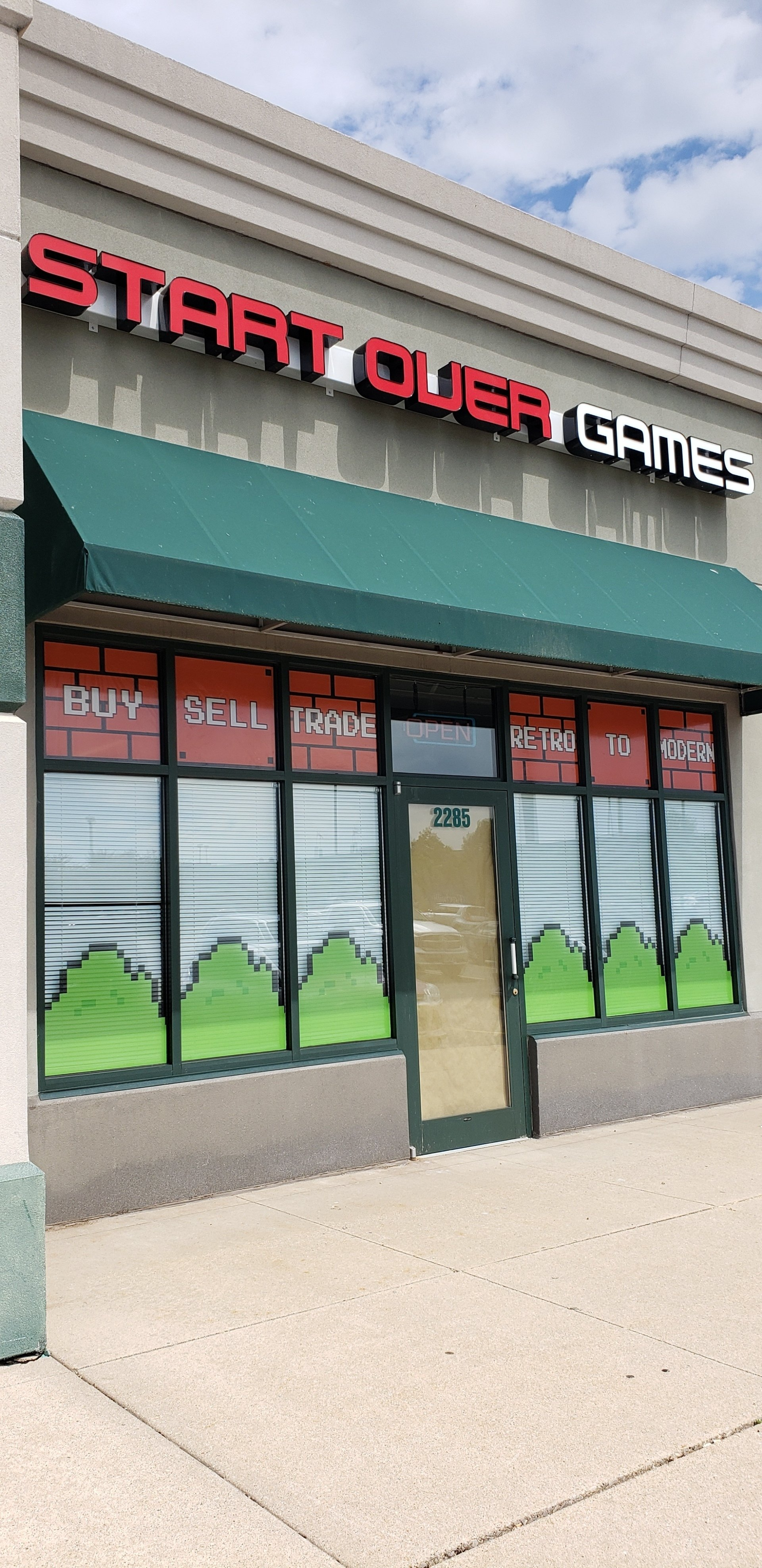 A store front with a green awning and a sign that says `` start over games ''.