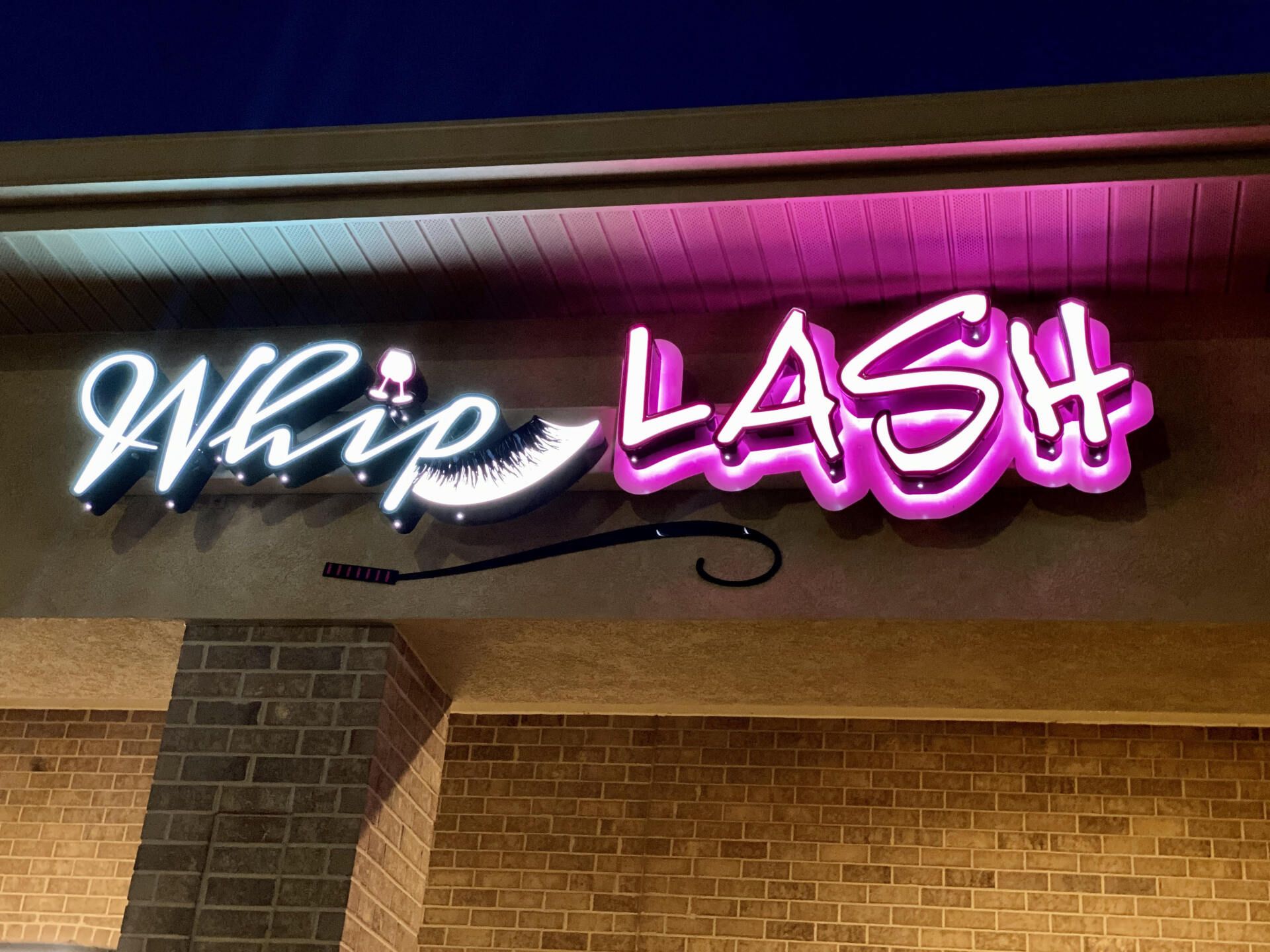 A neon sign for whip lash is lit up at night
