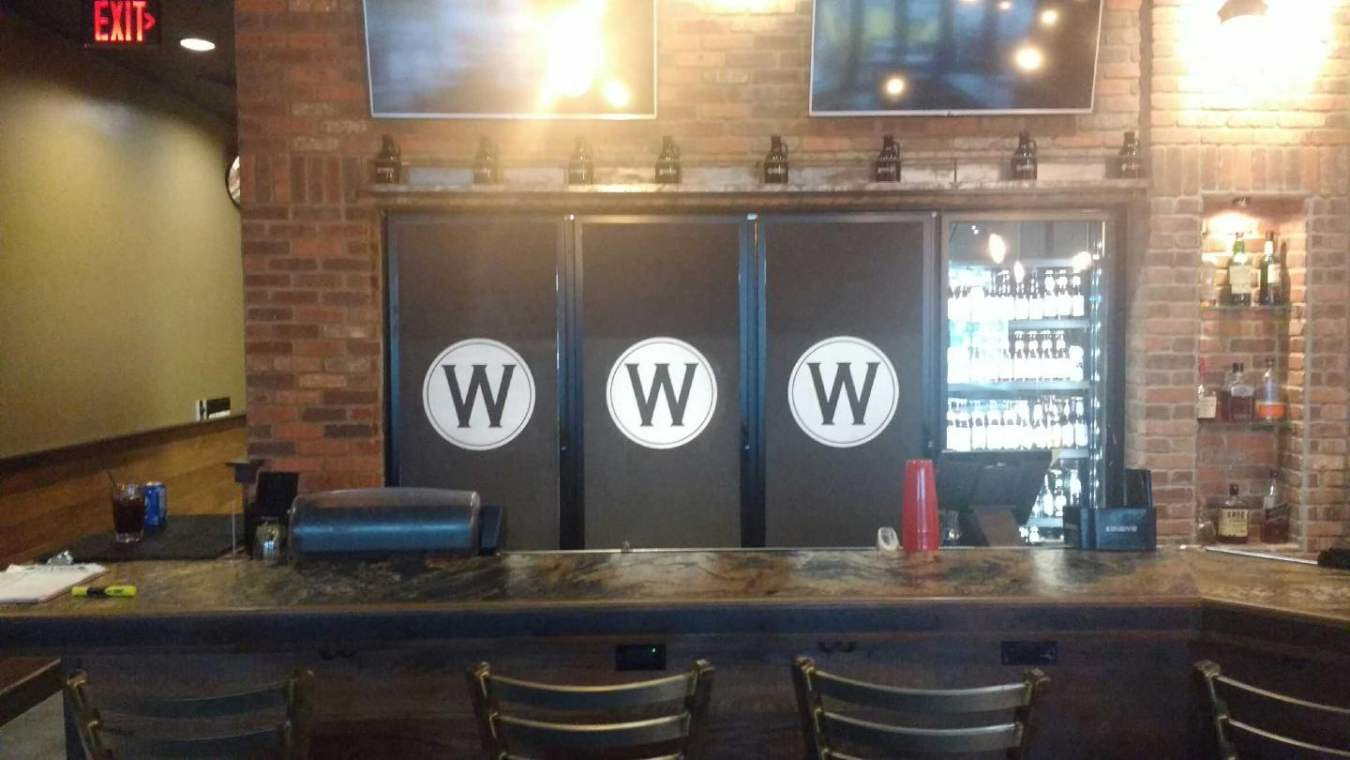 A bar with stools and a refrigerator in a restaurant.