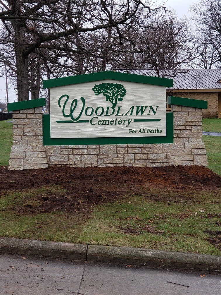 A sign for woodlawn cemetery is sitting on the side of the road.
