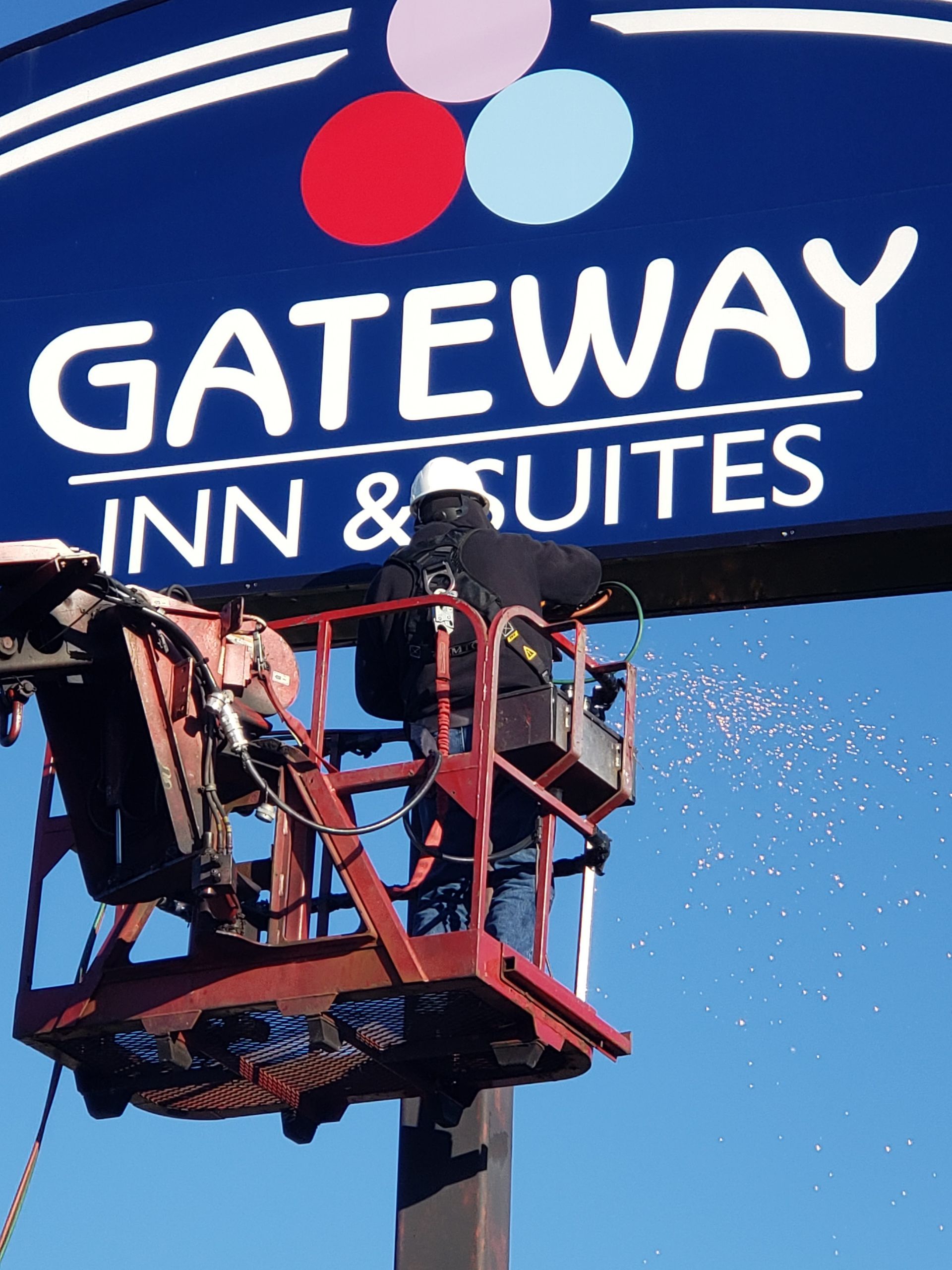 Worker on a lift beside Gateway Inn & Suites sign against a blue sky