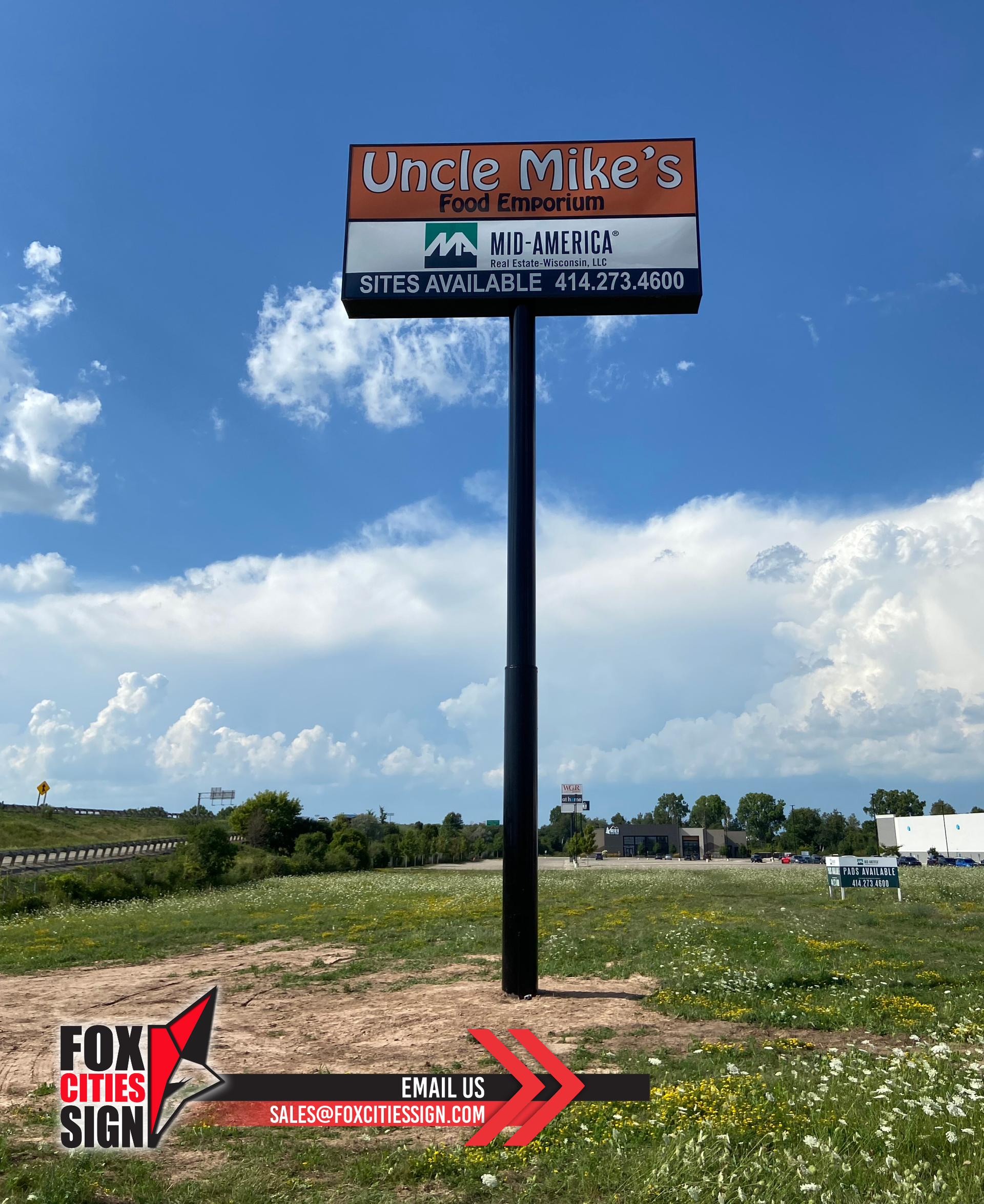 A billboard for uncle mike 's fried chicken is sitting in the middle of a field.