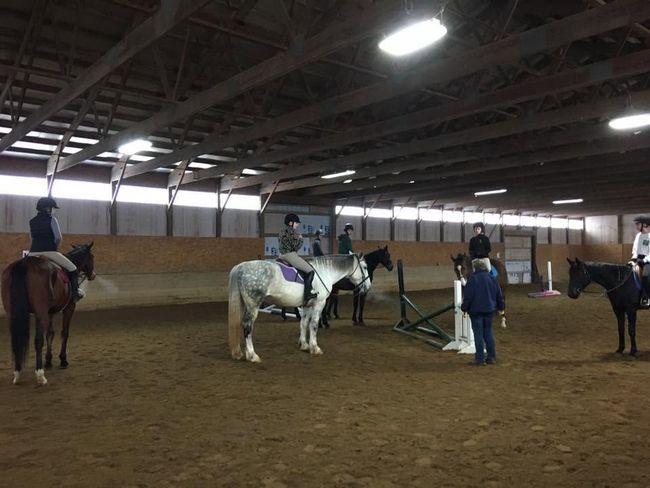 People riding horses in an indoor arena during a training lesson