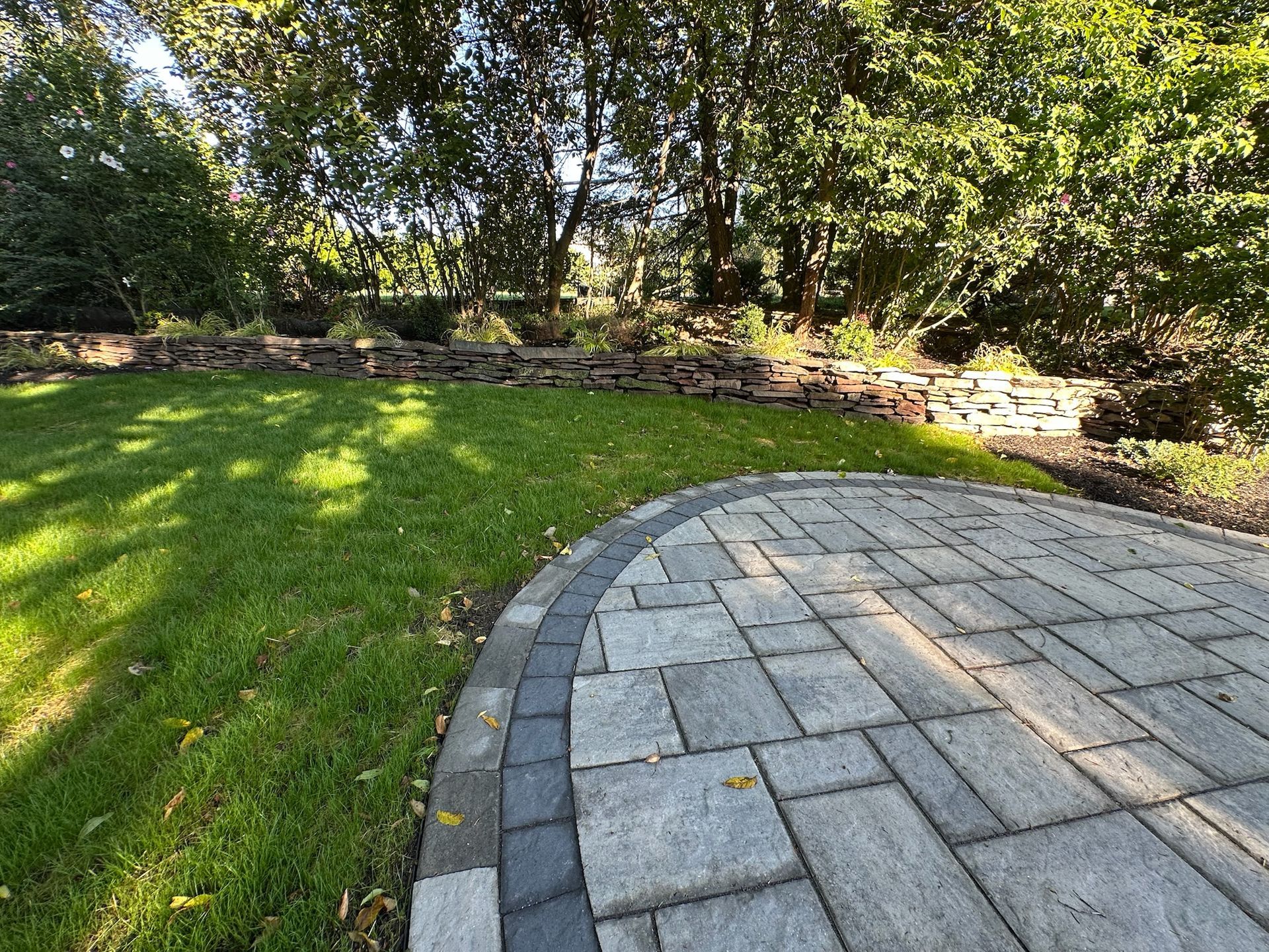 Patio with stone pavers next to a grassy lawn, trees in the background.