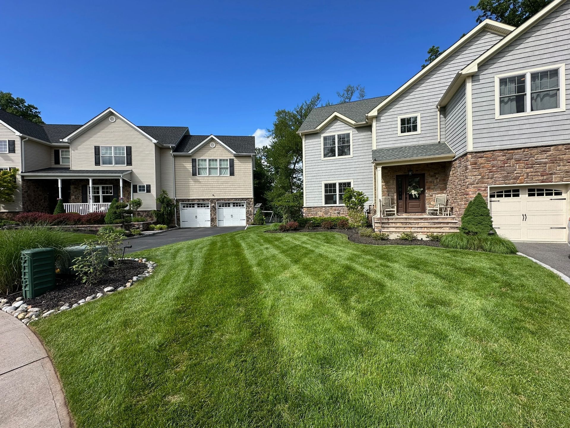 Row of suburban houses with neatly striped green lawns under a blue sky.