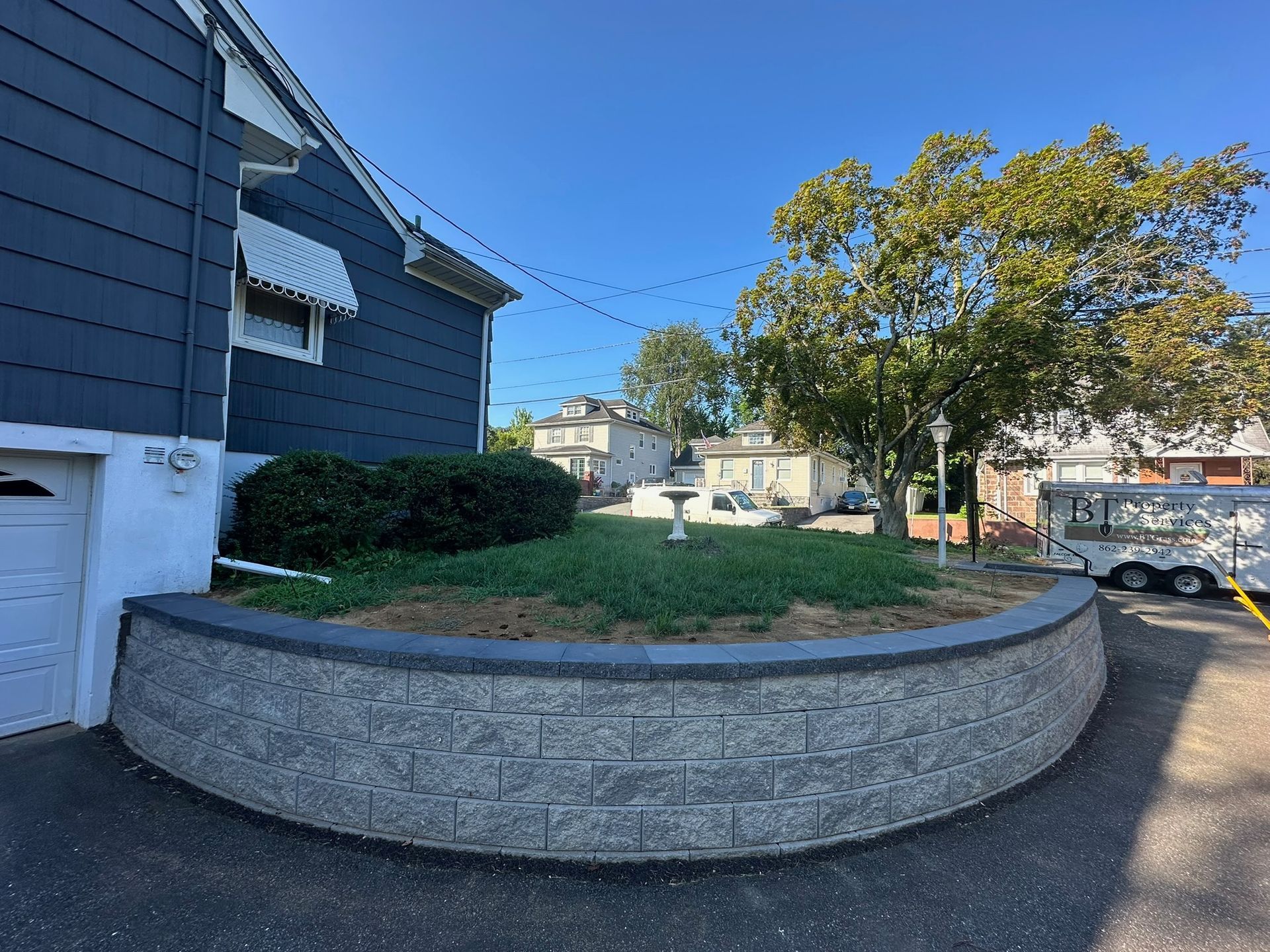 Curved retaining wall with a garden bed, house in the background, clear sky.