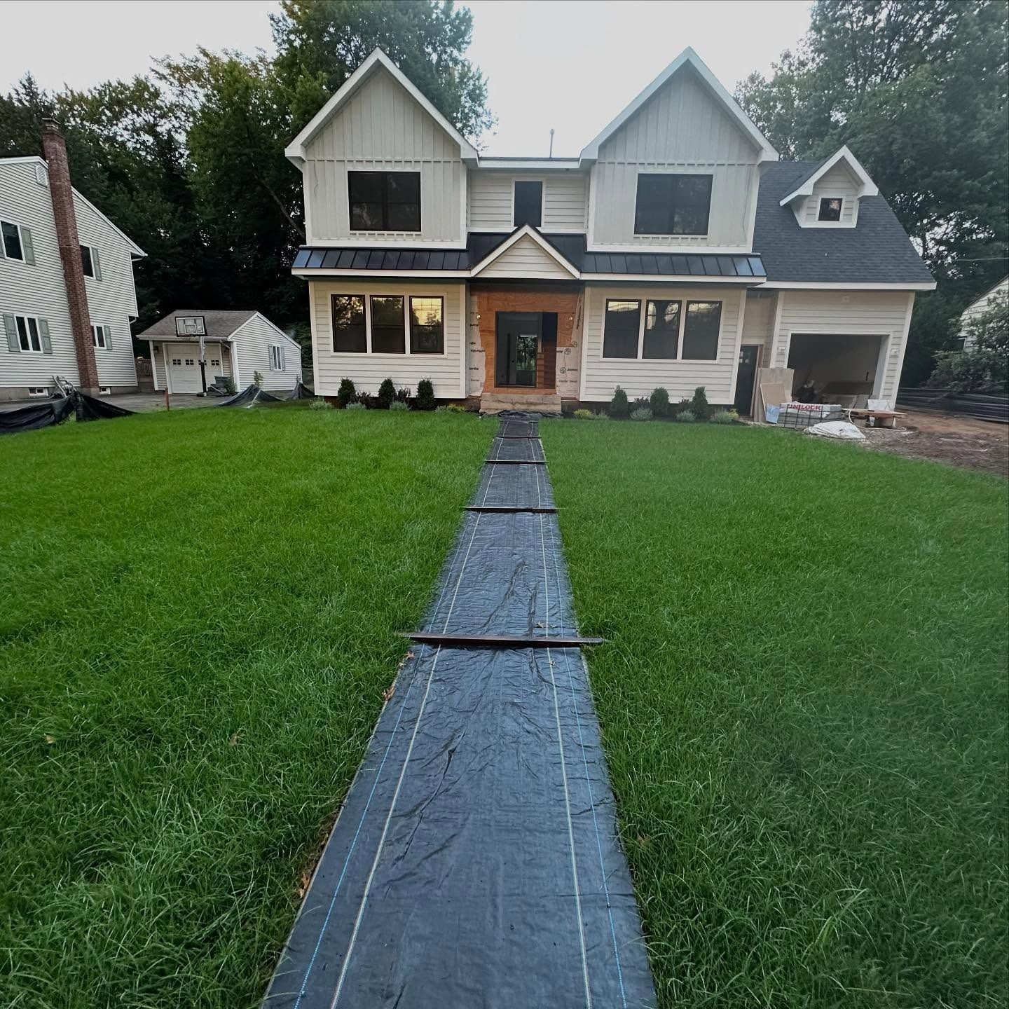 Two-story house with white siding and black windows, front door with a brown wood door, and black fabric path.