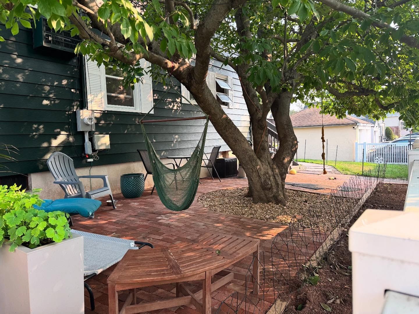 Patio with brick and wood surfaces, tree, hanging chair, and green house siding.