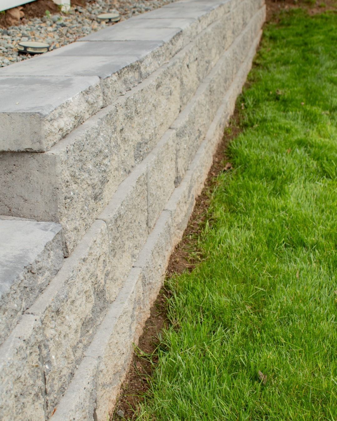 Gray retaining wall next to green grass lawn, steps visible.