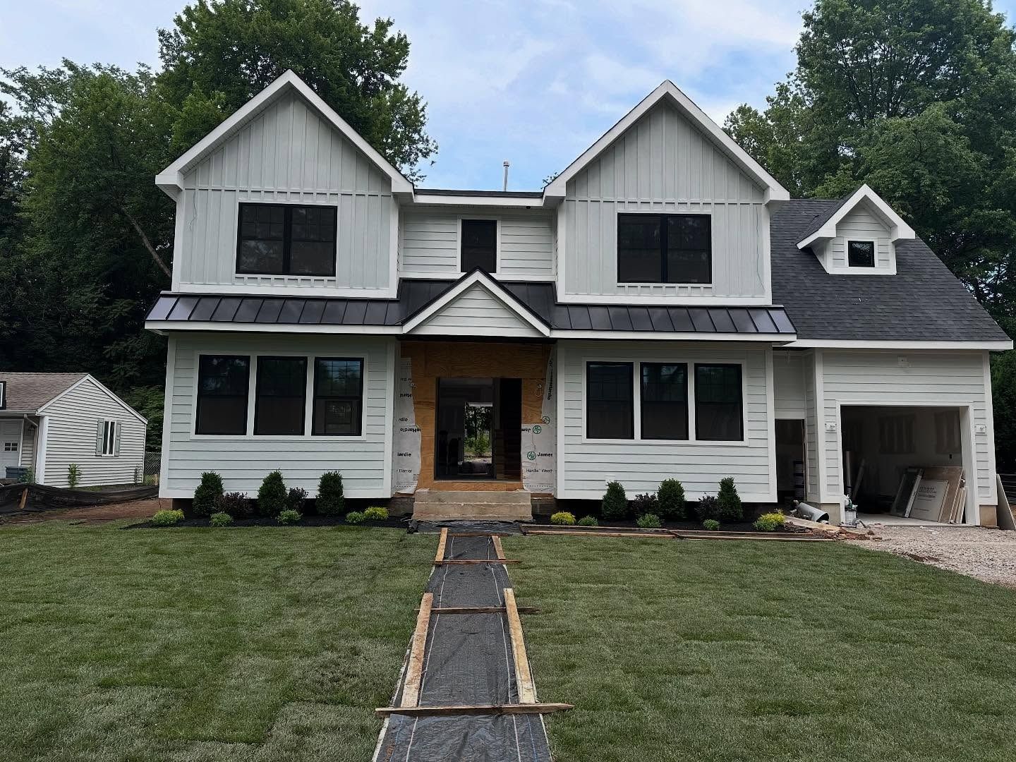 White house under construction with black windows and garage; green lawn.