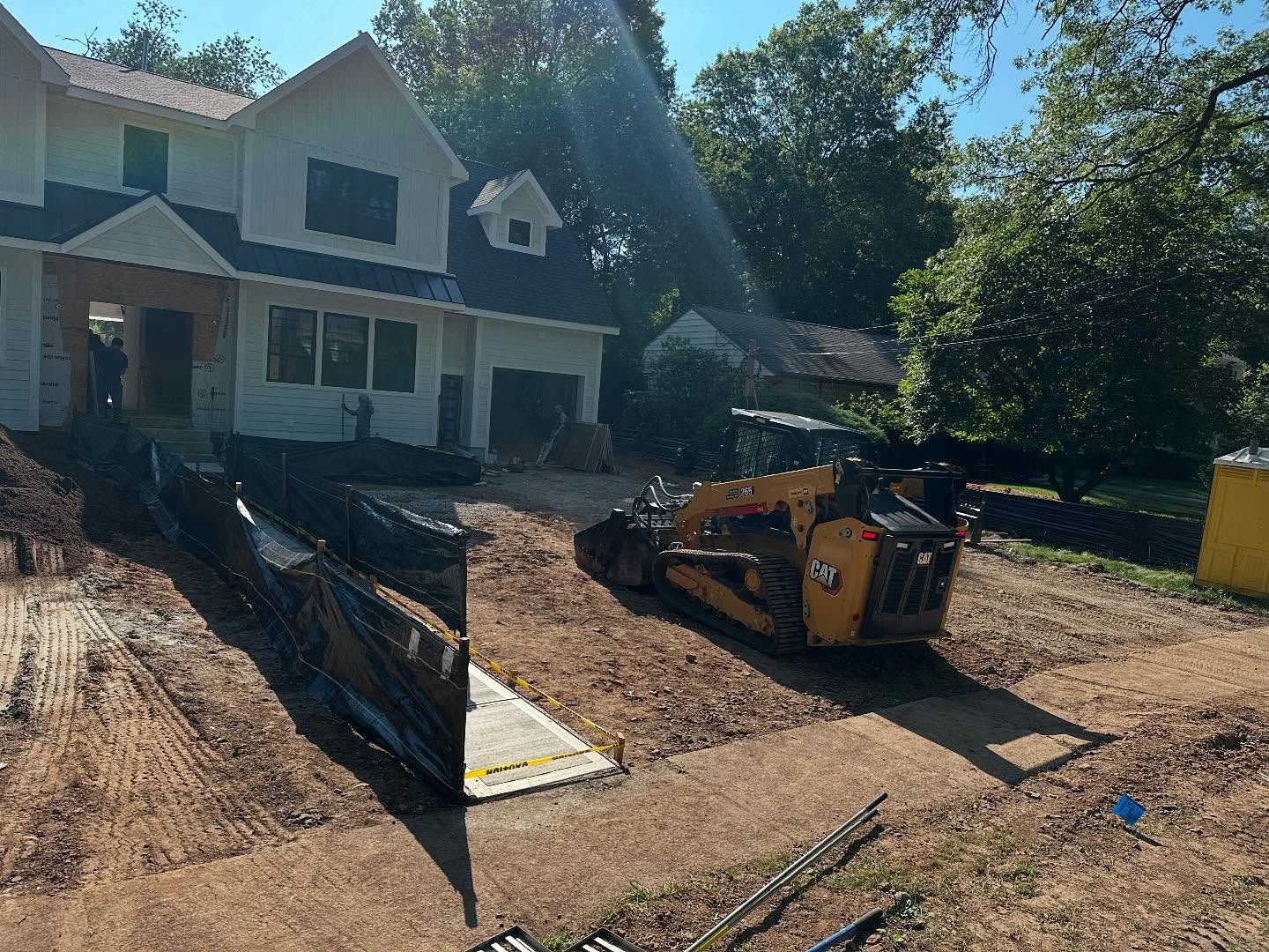 Yellow construction equipment in front of a house under construction on a sunny day.