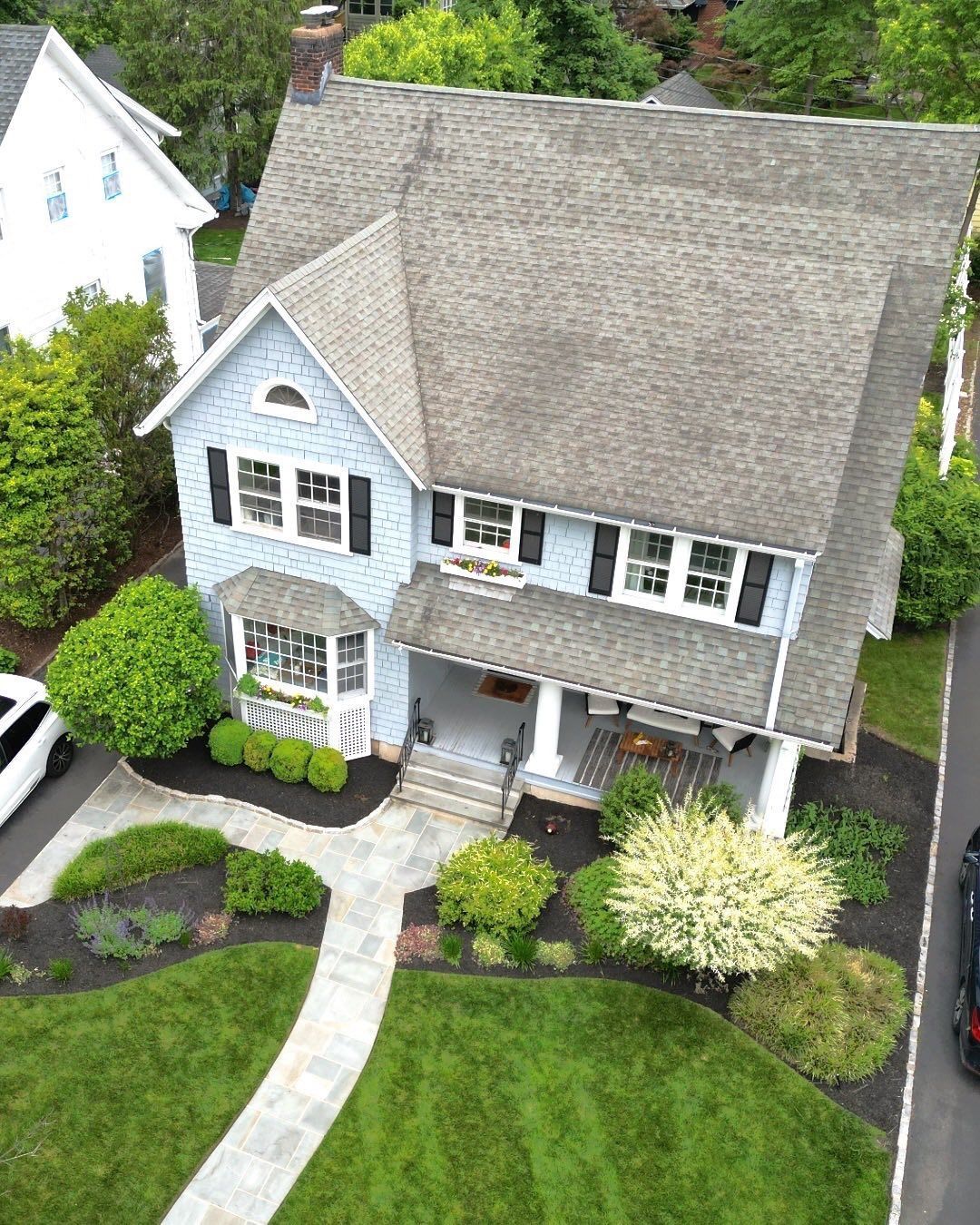 Blue two-story house with gray roof, black shutters, porch, and landscaped yard with walkway and lawn.