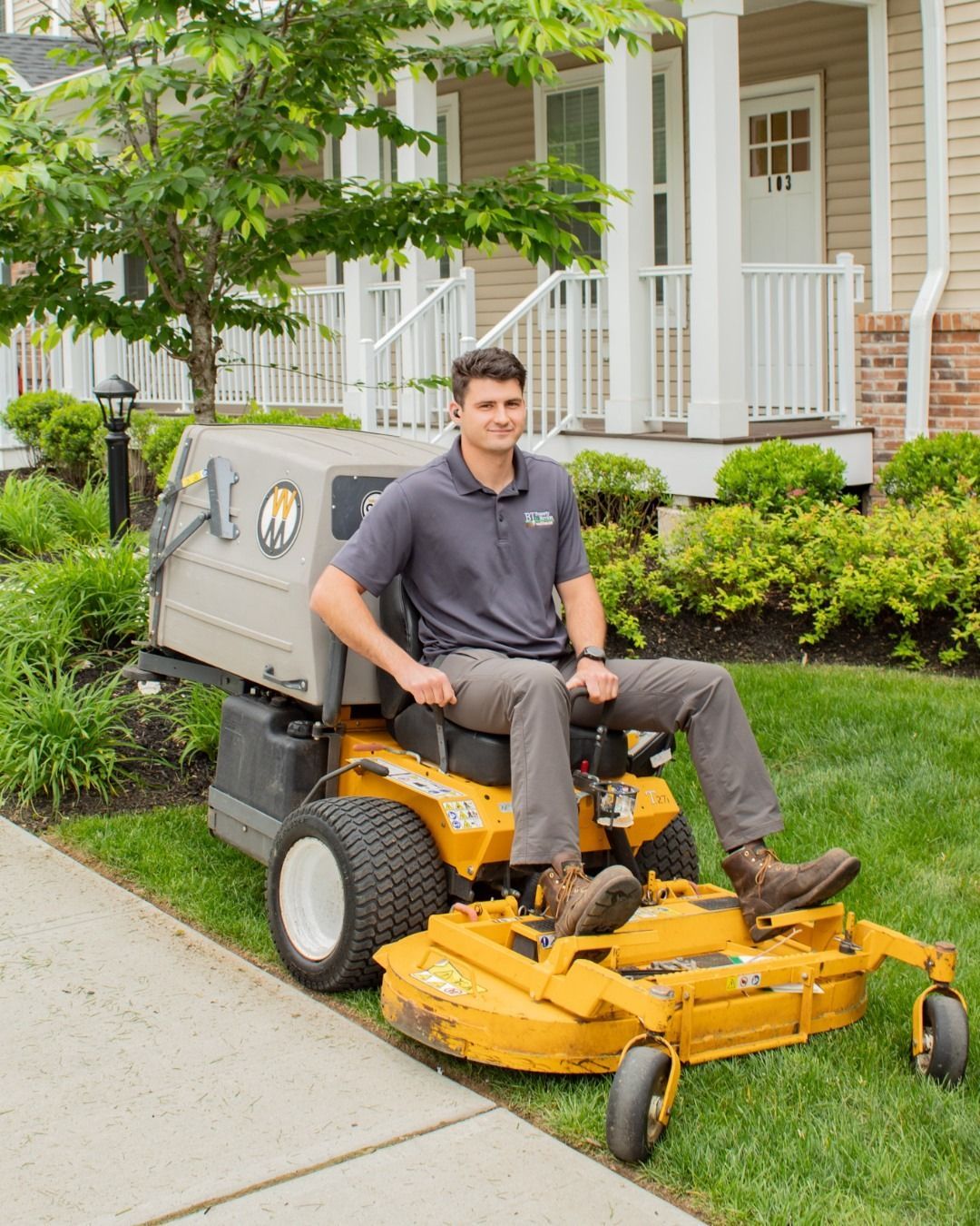 Man on riding lawnmower smiles in front of a house.