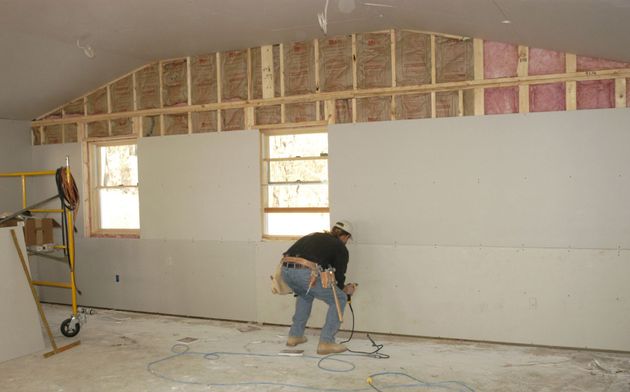 Man working in an unfinished room with exposed framing and drywall during renovation.