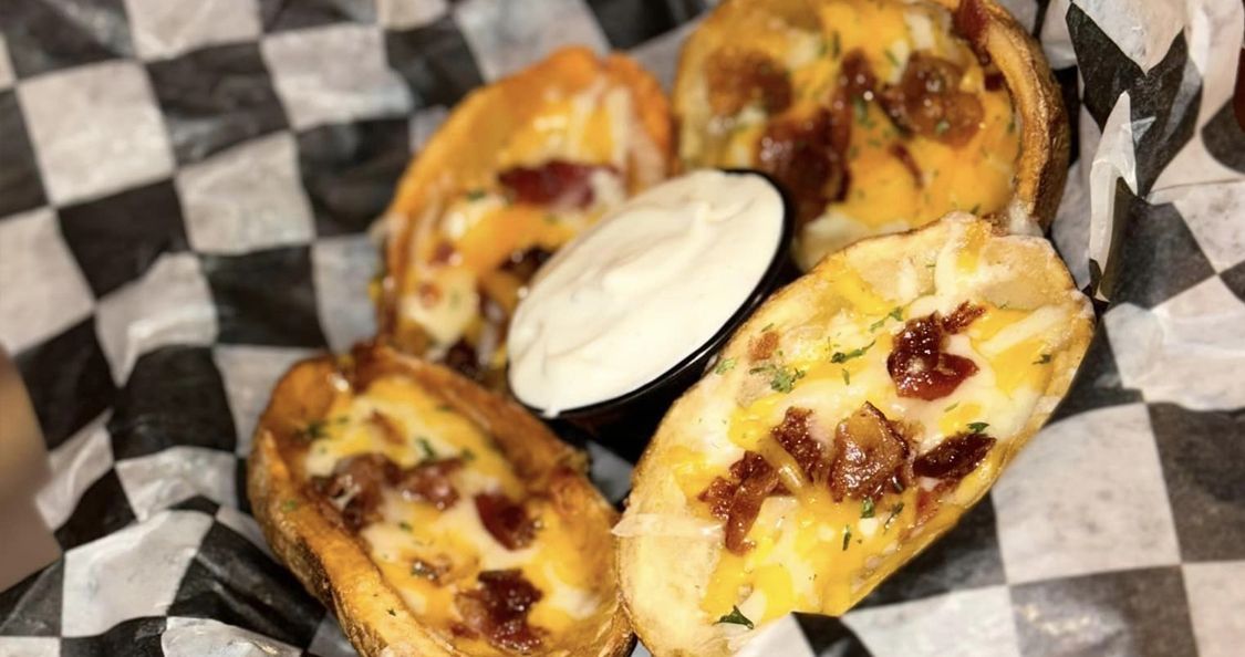 A basket of potato skins with sour cream and bacon on a checkered paper .