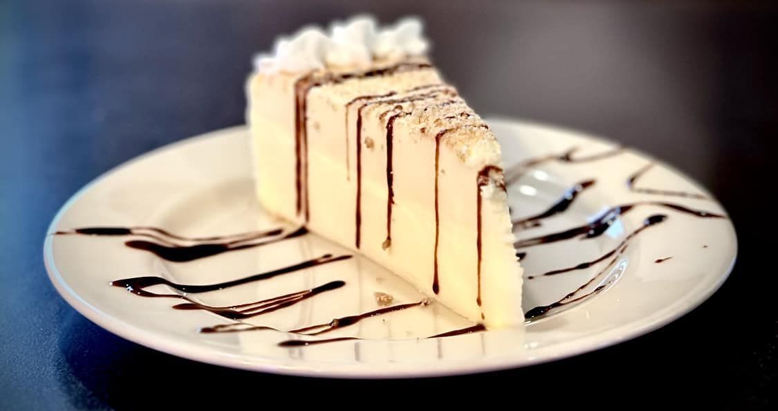 A slice of cheesecake on a white plate with chocolate sauce