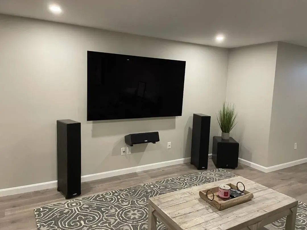 Modern living room with wall-mounted TV, tall speakers, patterned rug, and coffee table.