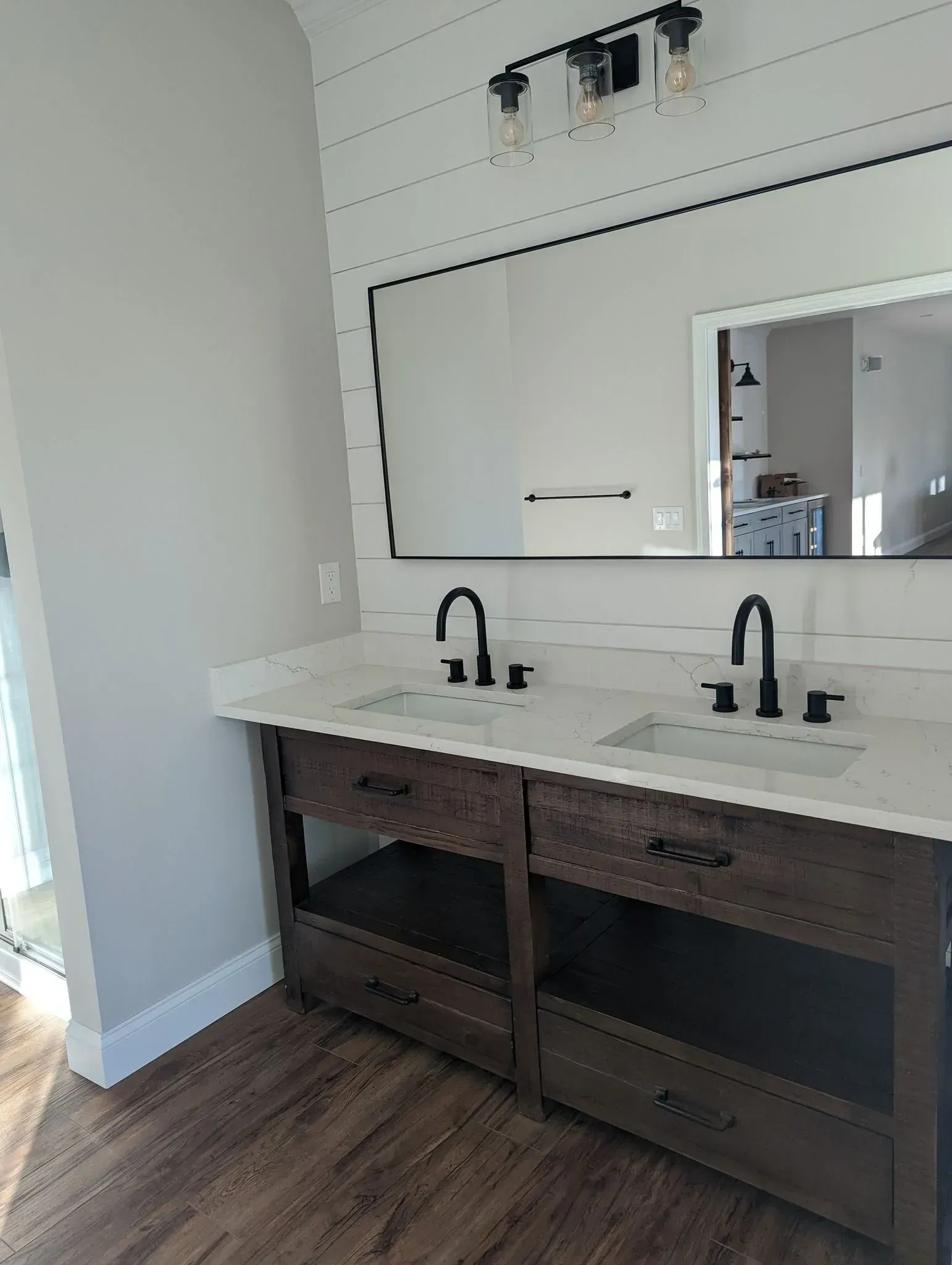 Modern bathroom vanity with double sinks, black faucets, large mirror, and wood cabinetry under white counters