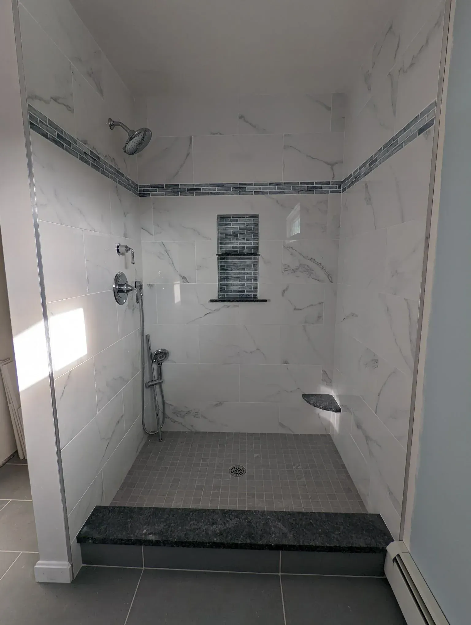 Empty tiled shower with a bench, white marble-style walls, and a small window.