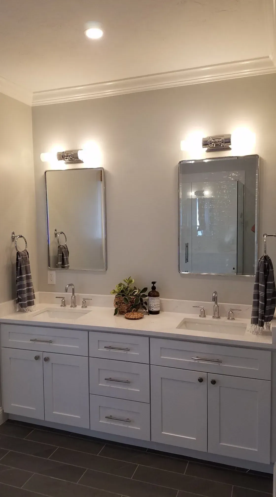 Modern bathroom vanity with double sinks, two mirrors, and wall sconces above a white cabinet.