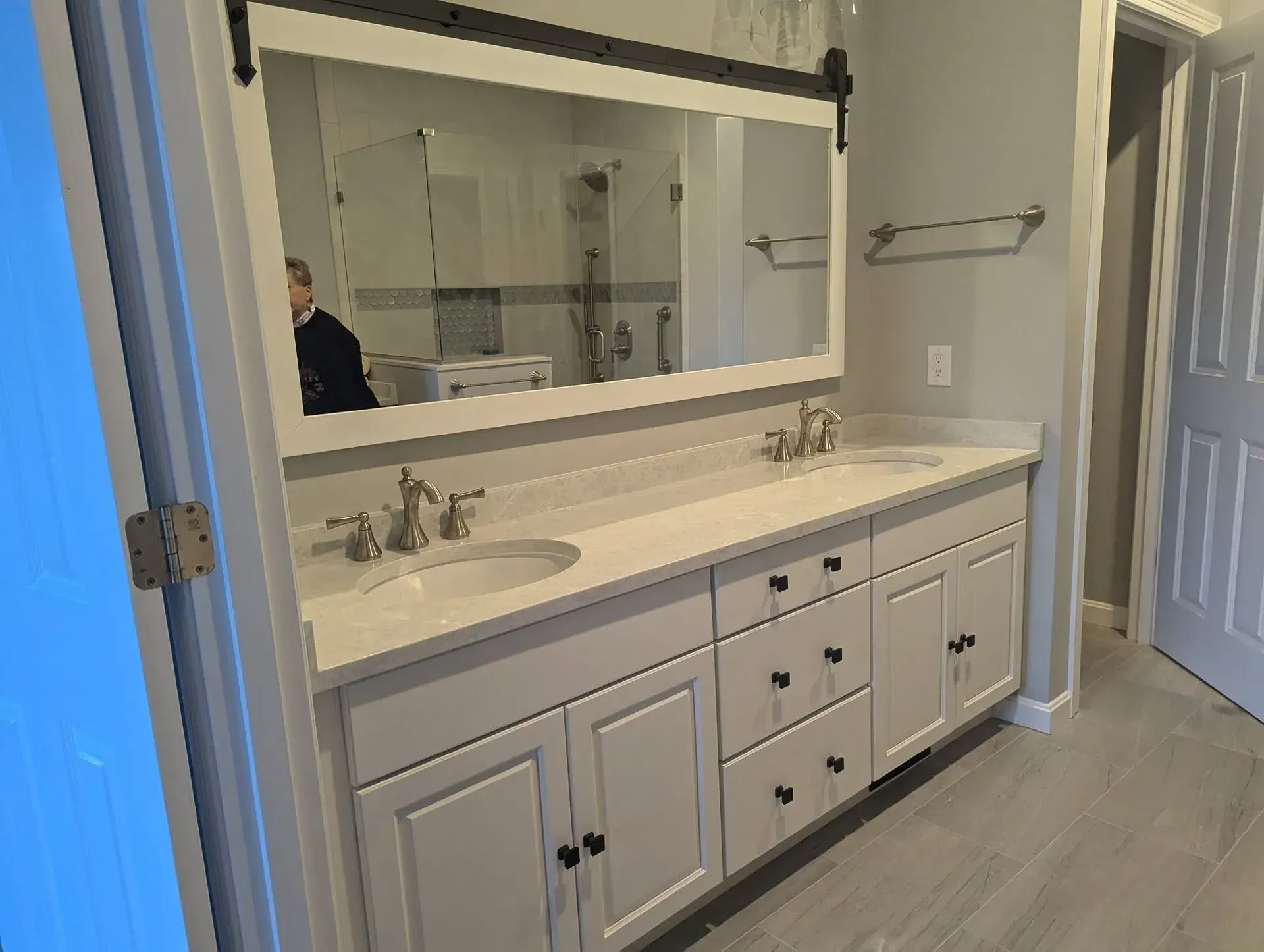 Modern bathroom vanity with double sinks, large mirror, and gray cabinetry by an open doorway