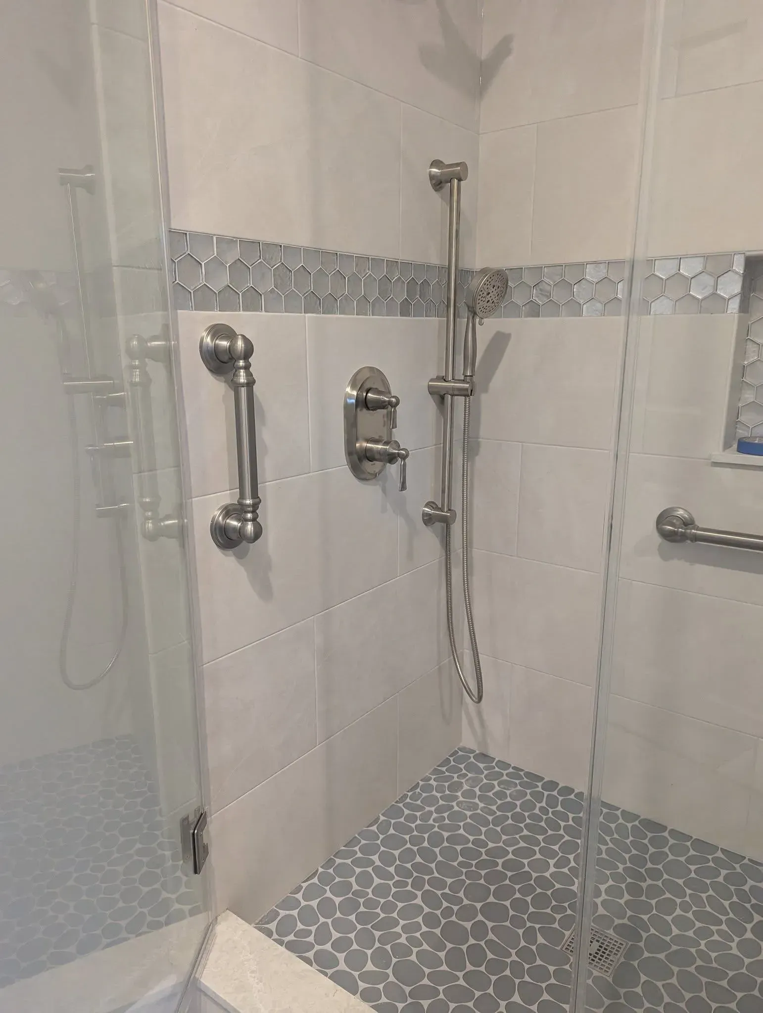 Walk-in shower with grab bars, handheld showerhead, and mosaic tile floor.