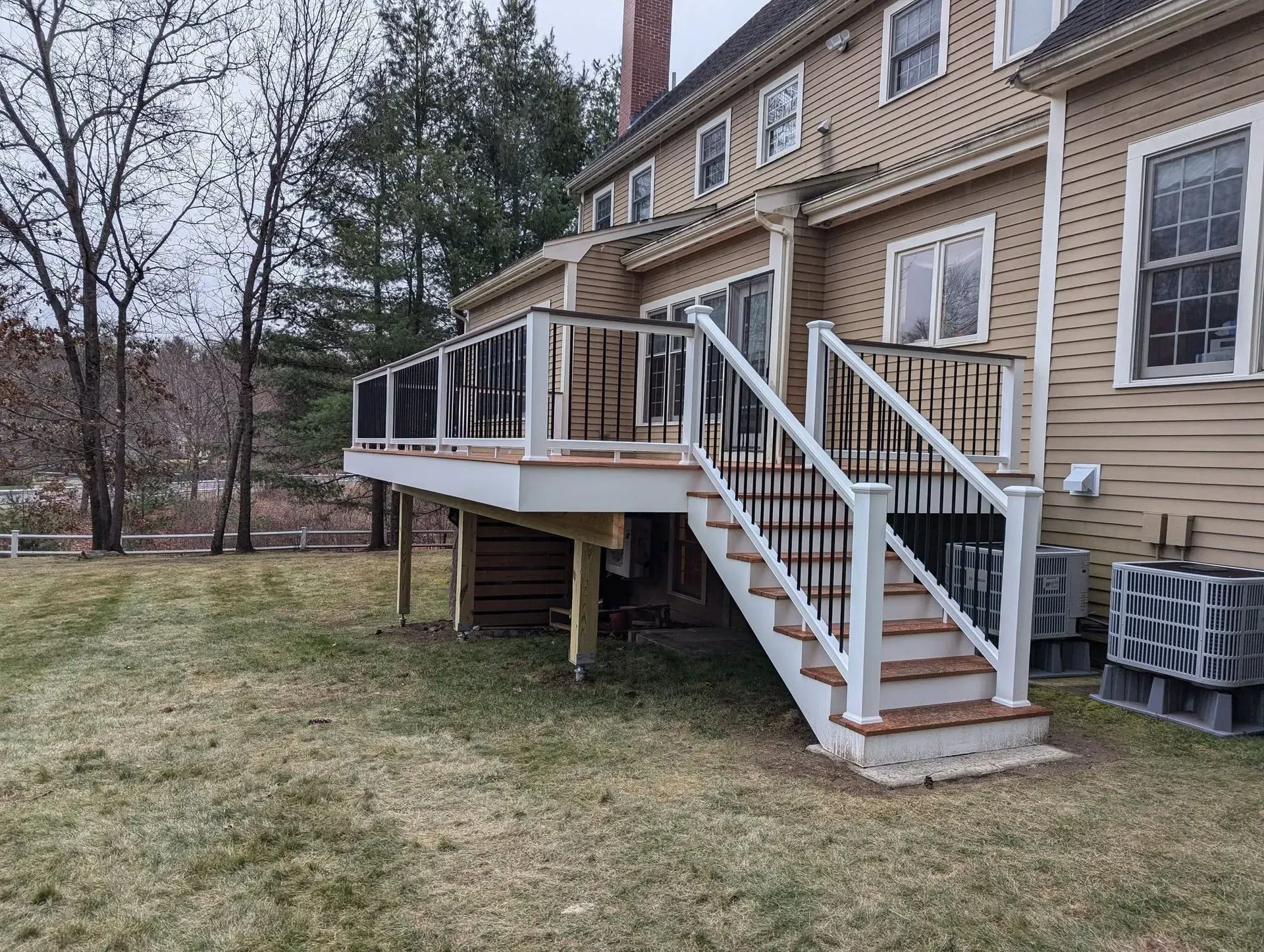 Backyard deck with white stairs and railings attached to a tan brick house
