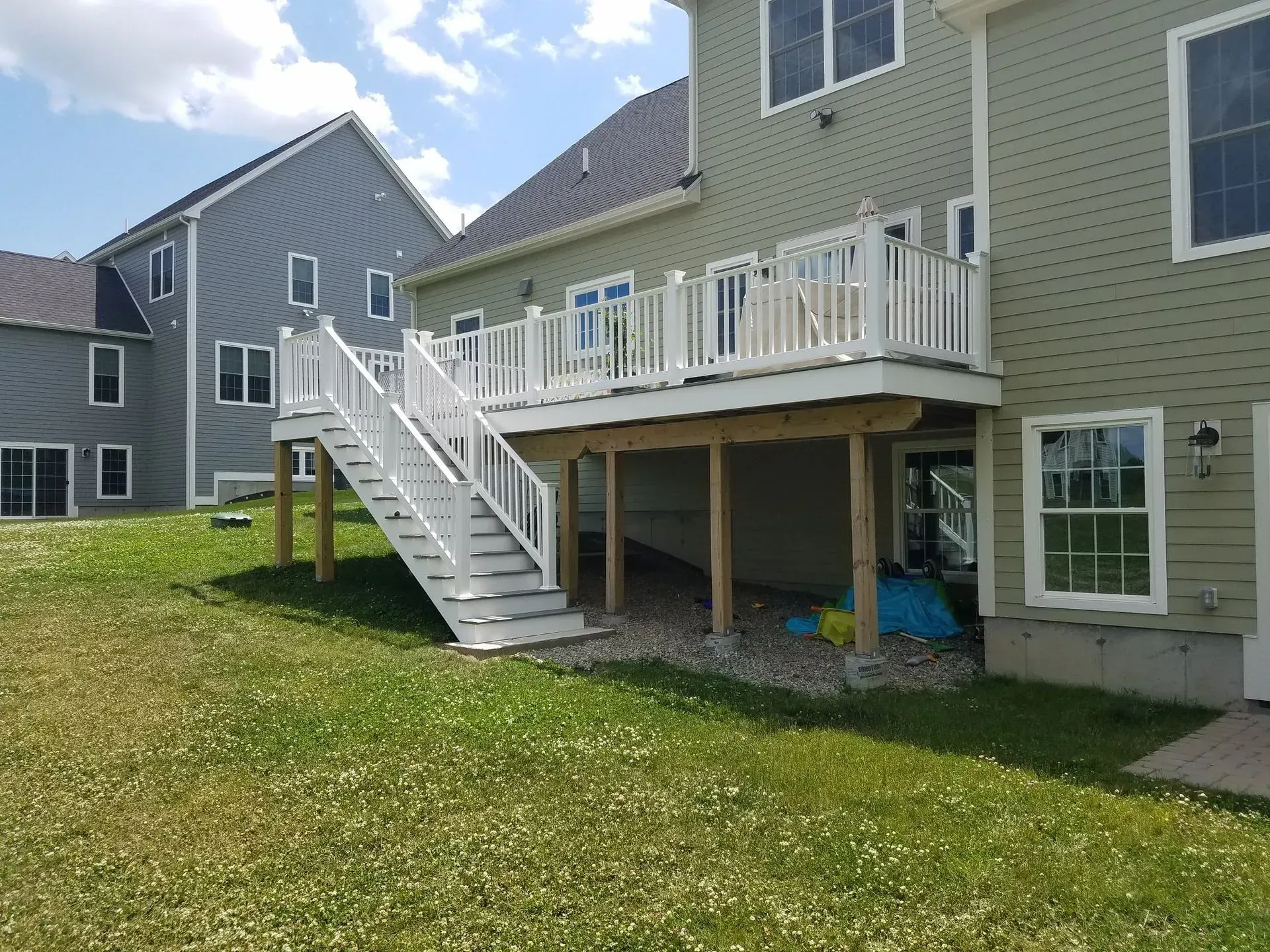 Backyard view of a raised deck with white stairs, railings, and a house on a grassy lawn.