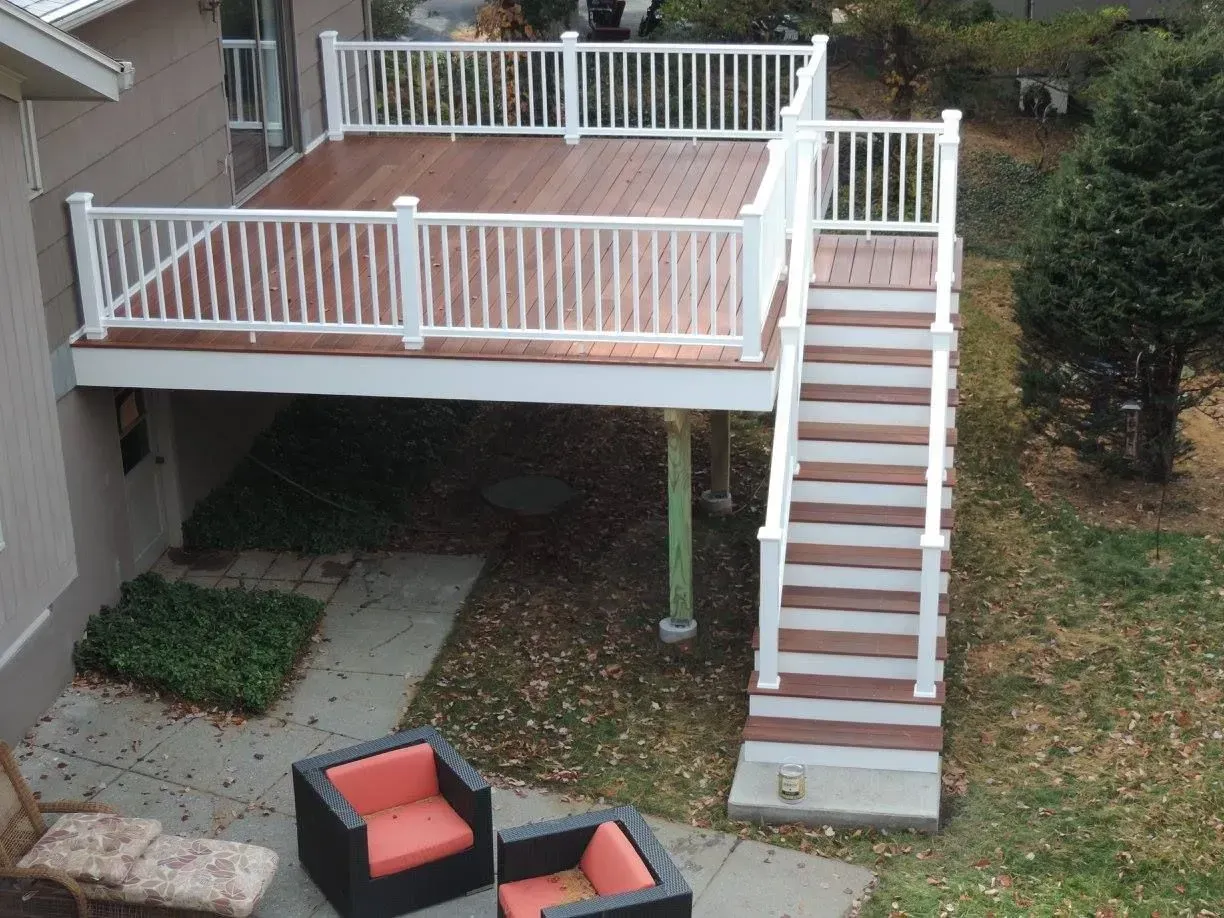 Backyard deck with white railings, stairs, and two red patio chairs underneath