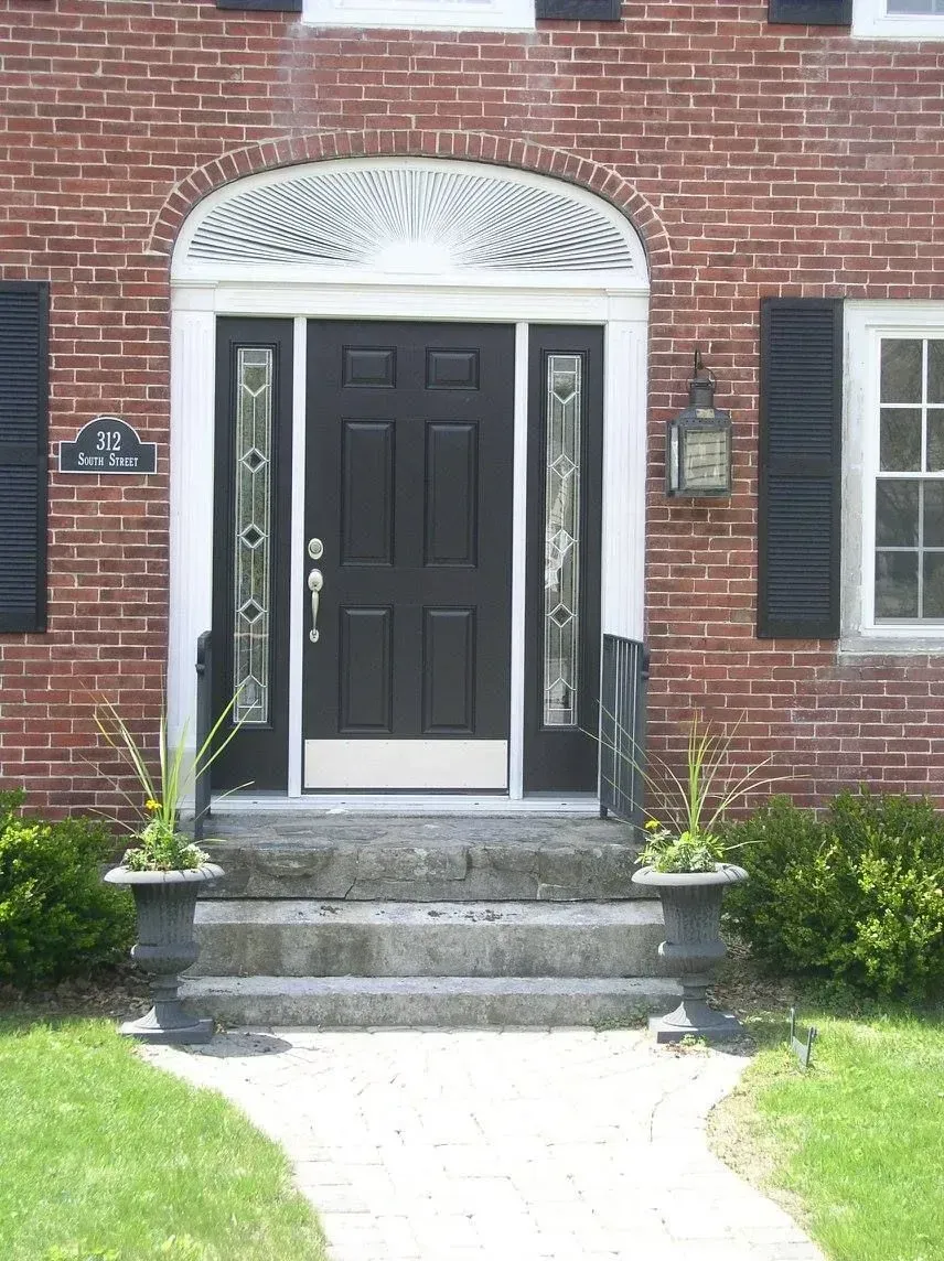 Brick building entrance with black door, stone steps, and white decorative archway above.