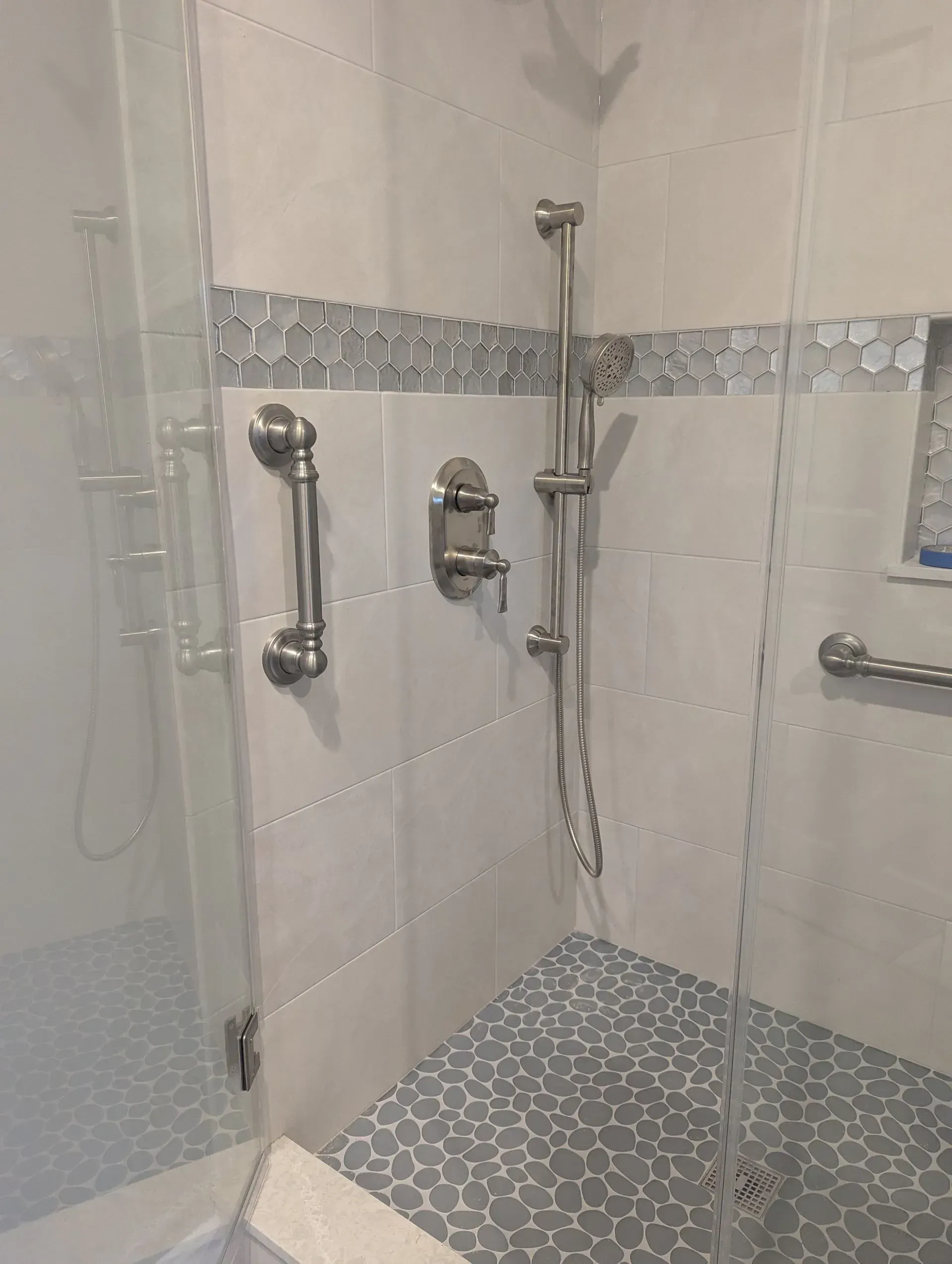 Accessible shower with grab bars, handheld showerhead, fold-down seat, and patterned tile walls and floor